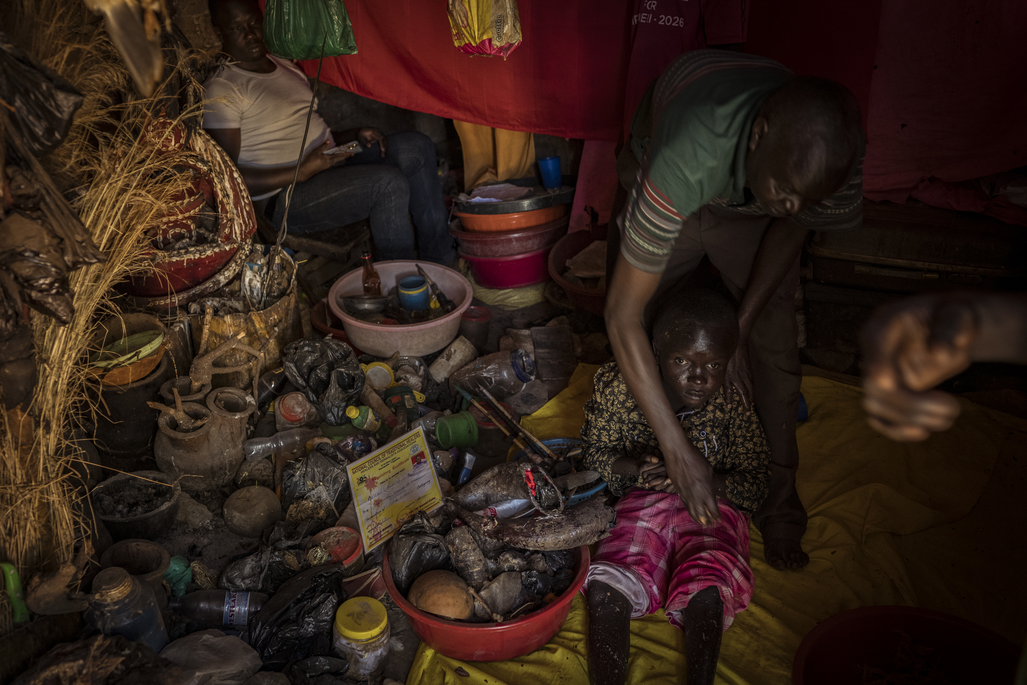 Omalera, Soroti District, Uganda. Local Witch doctor Robert Apedu treats Noah Oyara,17. Noah has no use of his legs and also lives with hydrocephalus. Robert treated these conditions by rubbing a paste of water and plant matter into Noahs skin. While he is well known in the area as a witch doctor, he understands the negative connotation surrounding his profession so like many others he refers to himself as a 'traditional healer or herbalist'. [Christopher Hopkins/Al Jazeera]