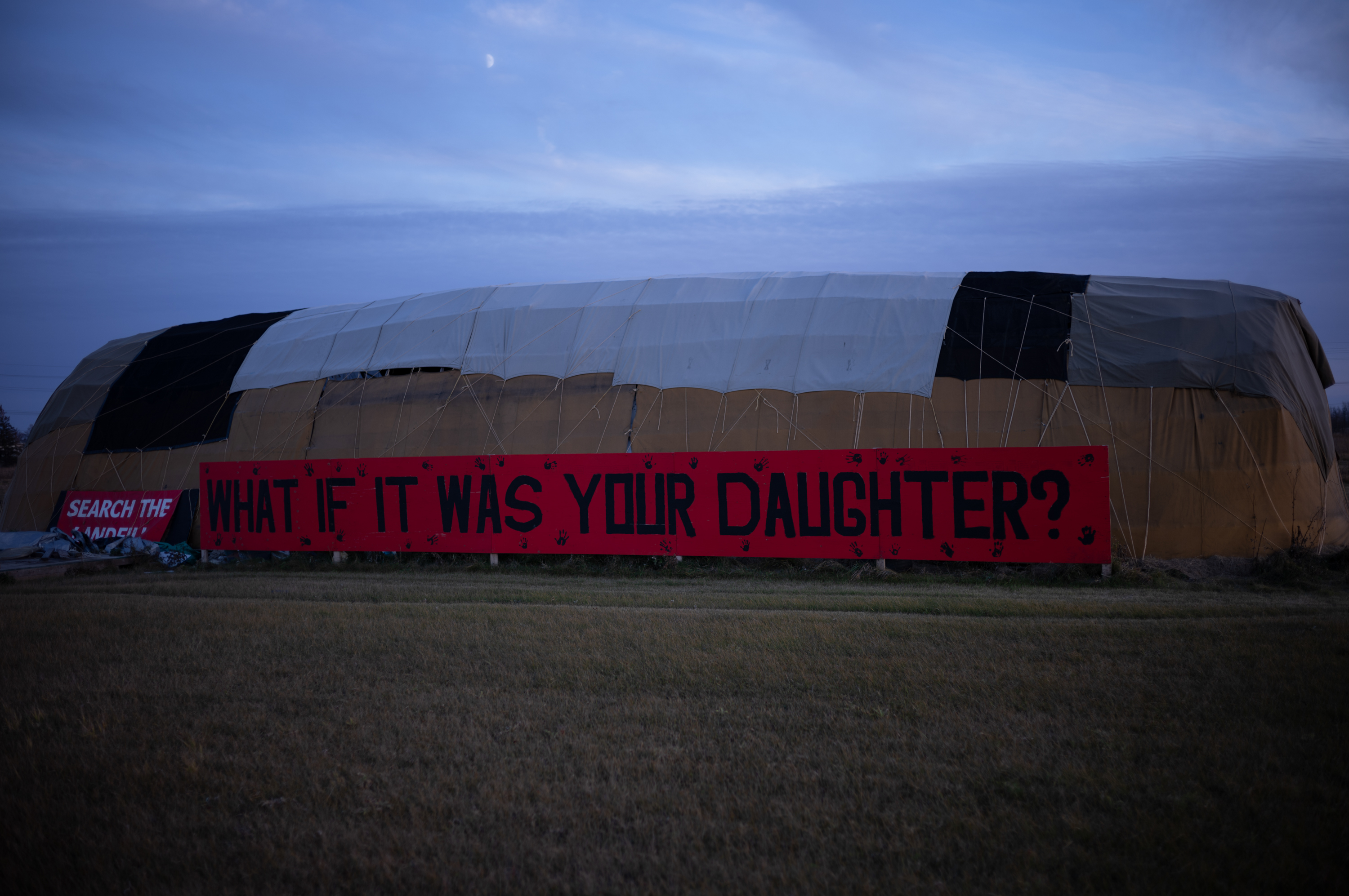 A large tent encampment is seen just before sunset. A long read banner along the side of the tent reads: What would you do if it was your daughter?