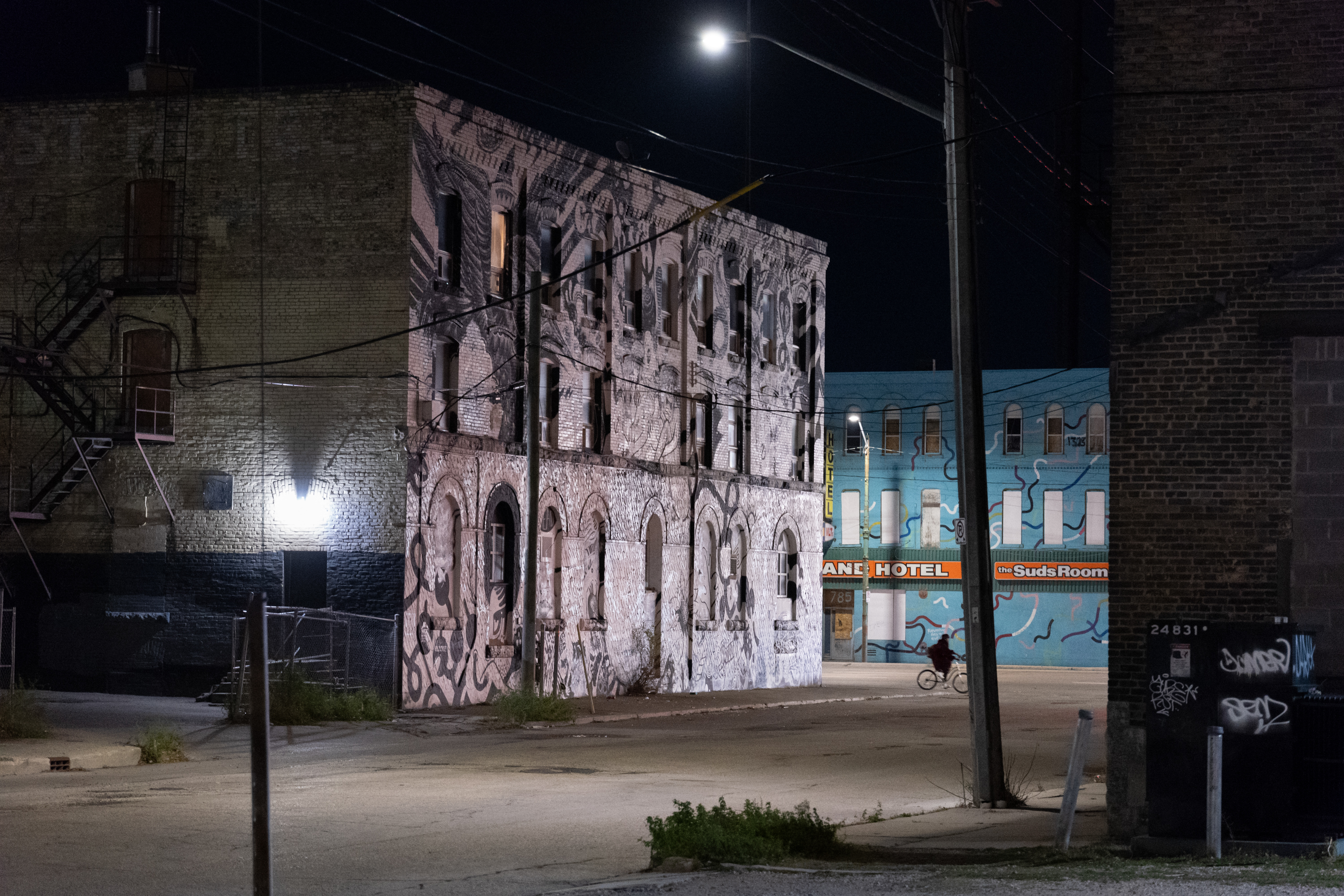 A grey building with boarded up windows is seen by an empty road with a lamppost