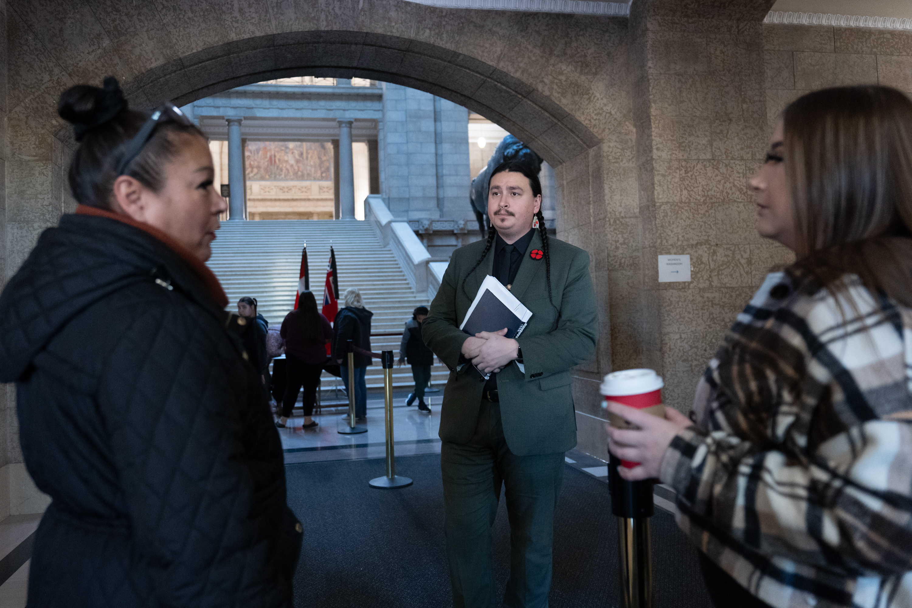 Three people - two women and a man - stand talking in front of a stone archway inside a large building