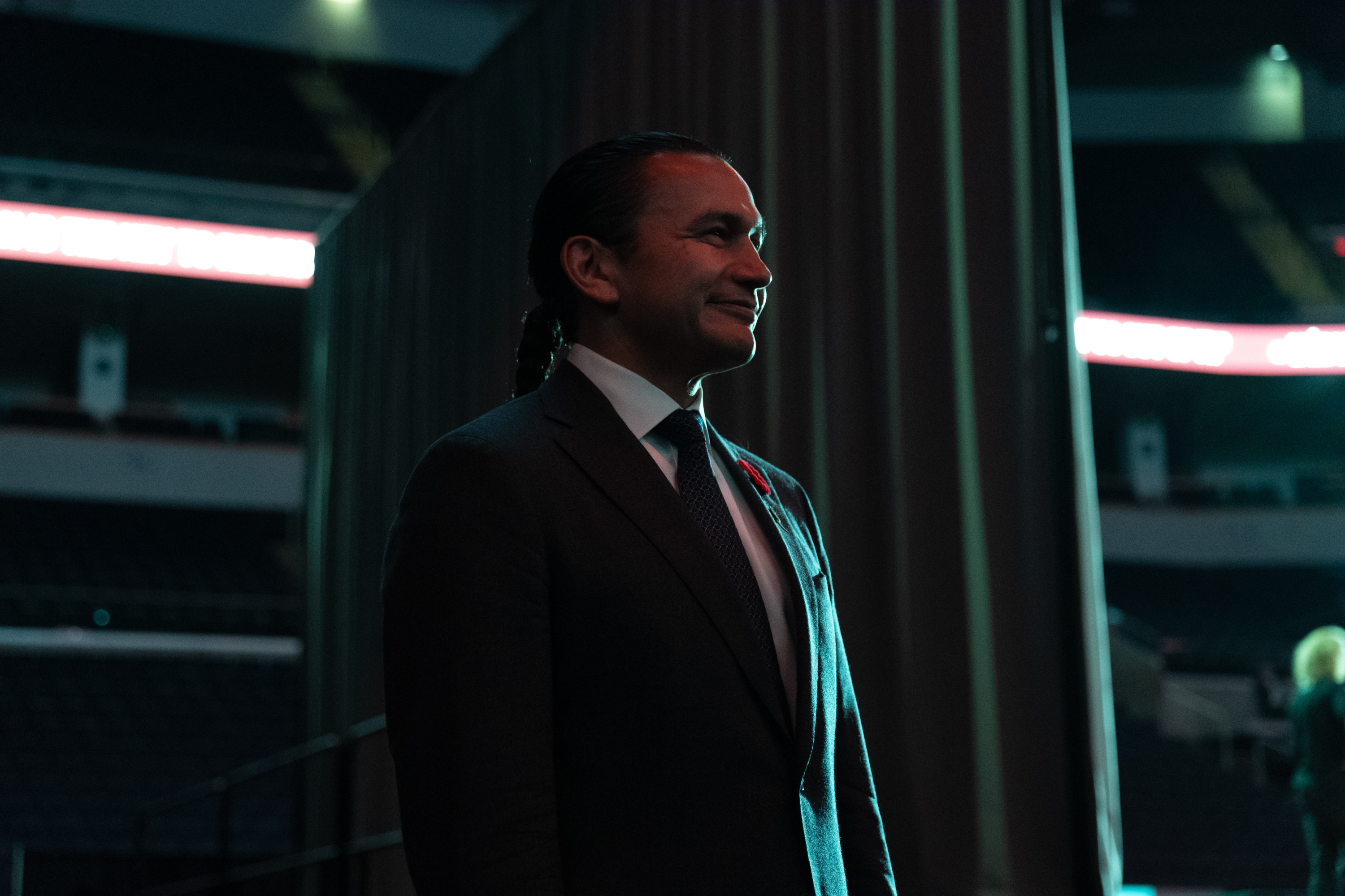 Wab Kinew stands by a curtain, wearing a suit and tie