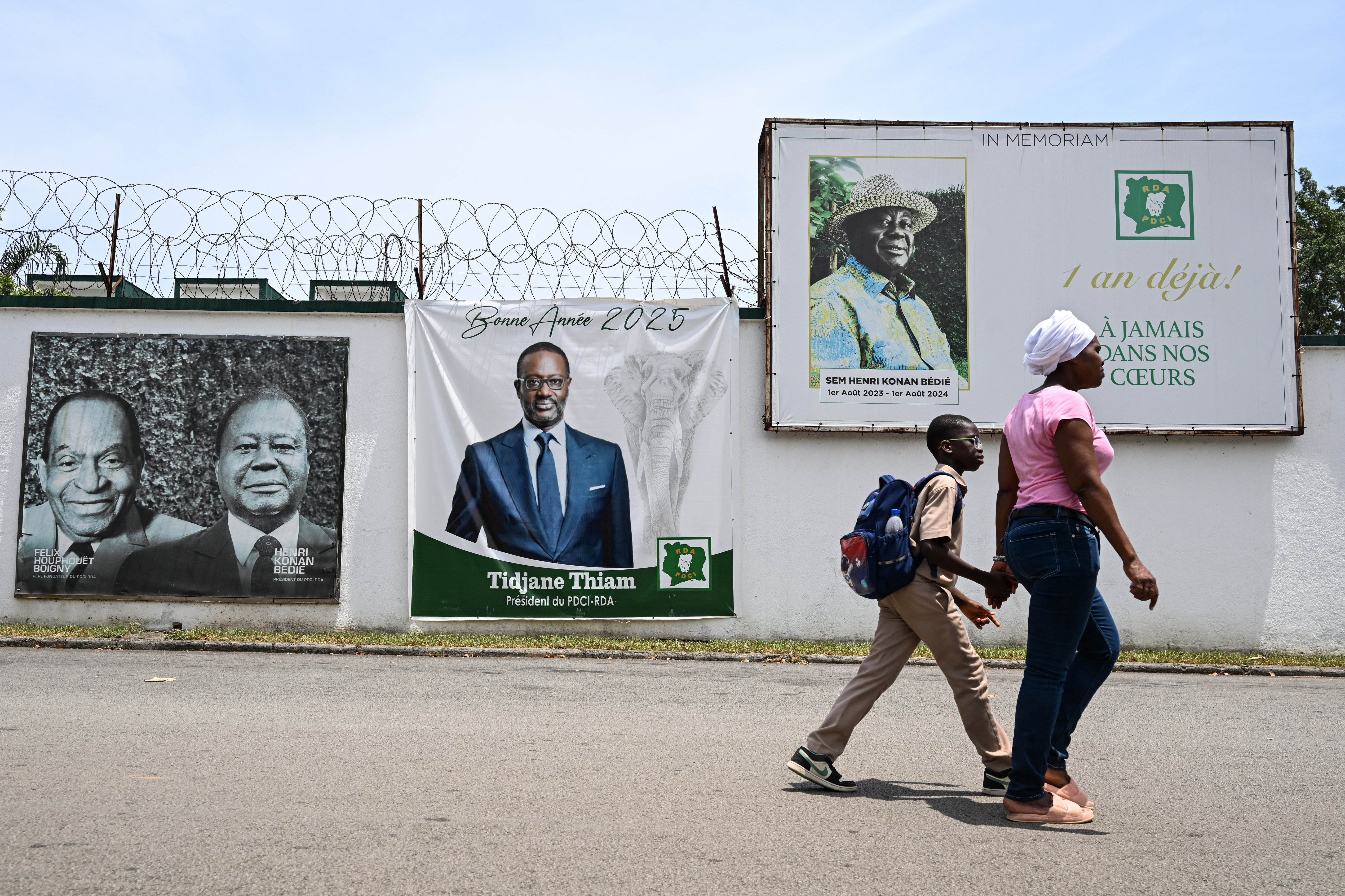 Pedestrians walk past an image of former Ivorian presidential candidate Tidjane Thiam in Abidjan on April 16, 2025. [Issouf Sanogo/AFP]