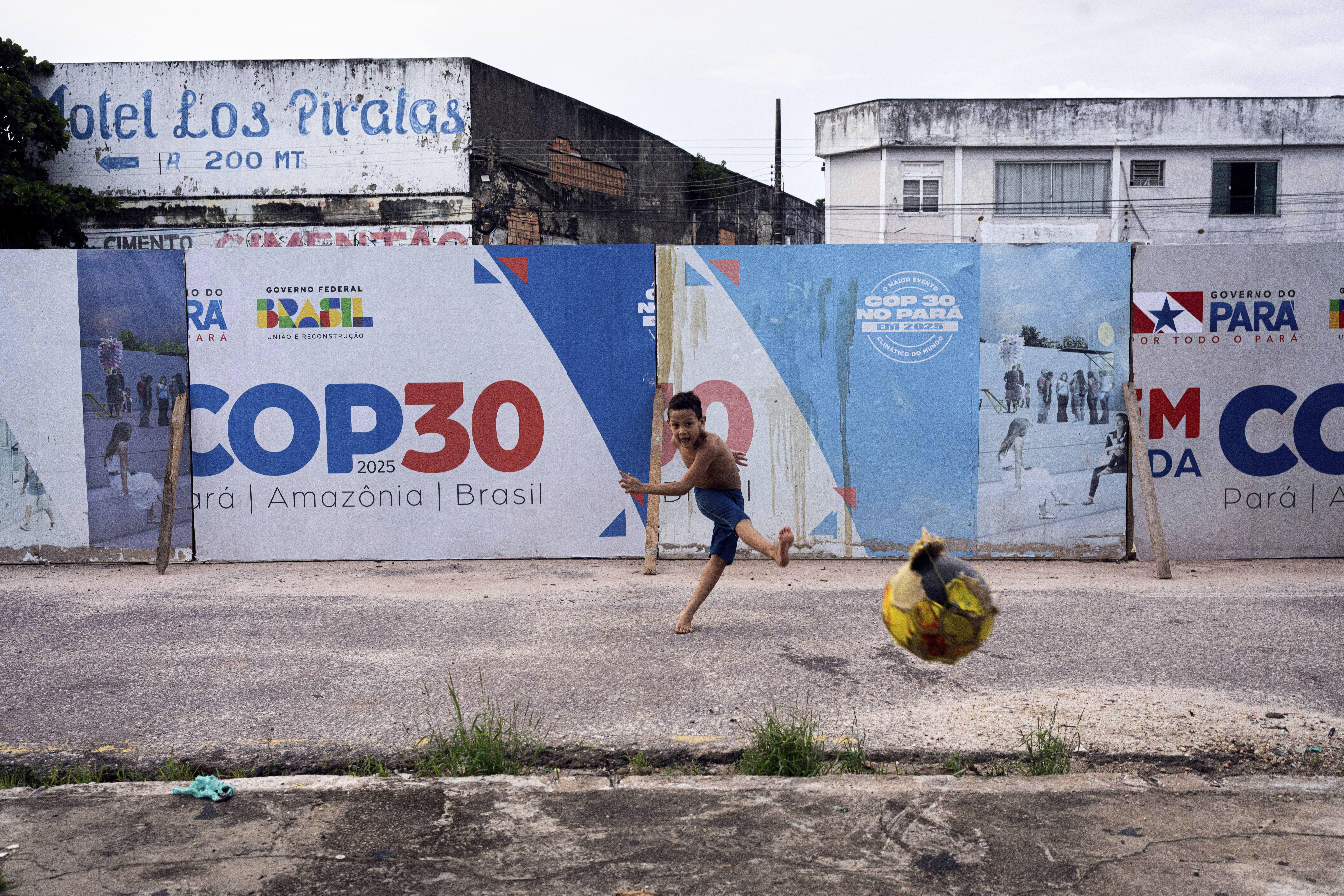 A boy kicks a soccer ball near signage for the COP30 UN Climate Conference in Belem, Brazil [File: Jorge Saenz/AP]