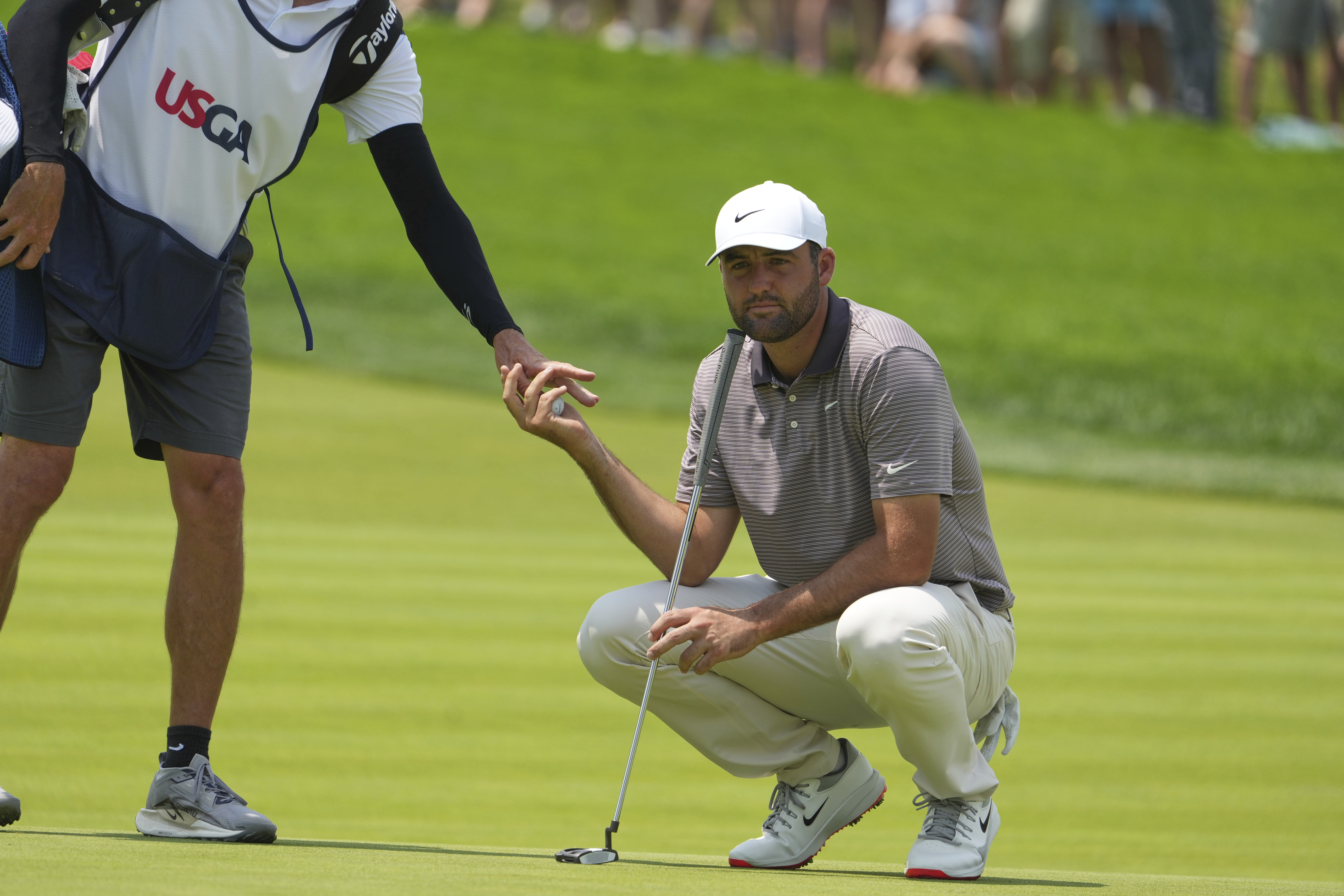 Caddie Ted Scott, left, hands a ball to Scottie Scheffler on the first green during the first round of the U.S. Open