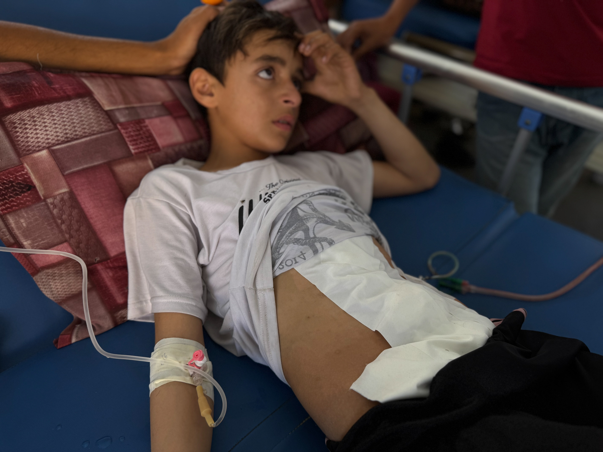 Yazan Muslet, a thin 13-year-old, lies on a hospital bed with a big white bandage holding his belly together.