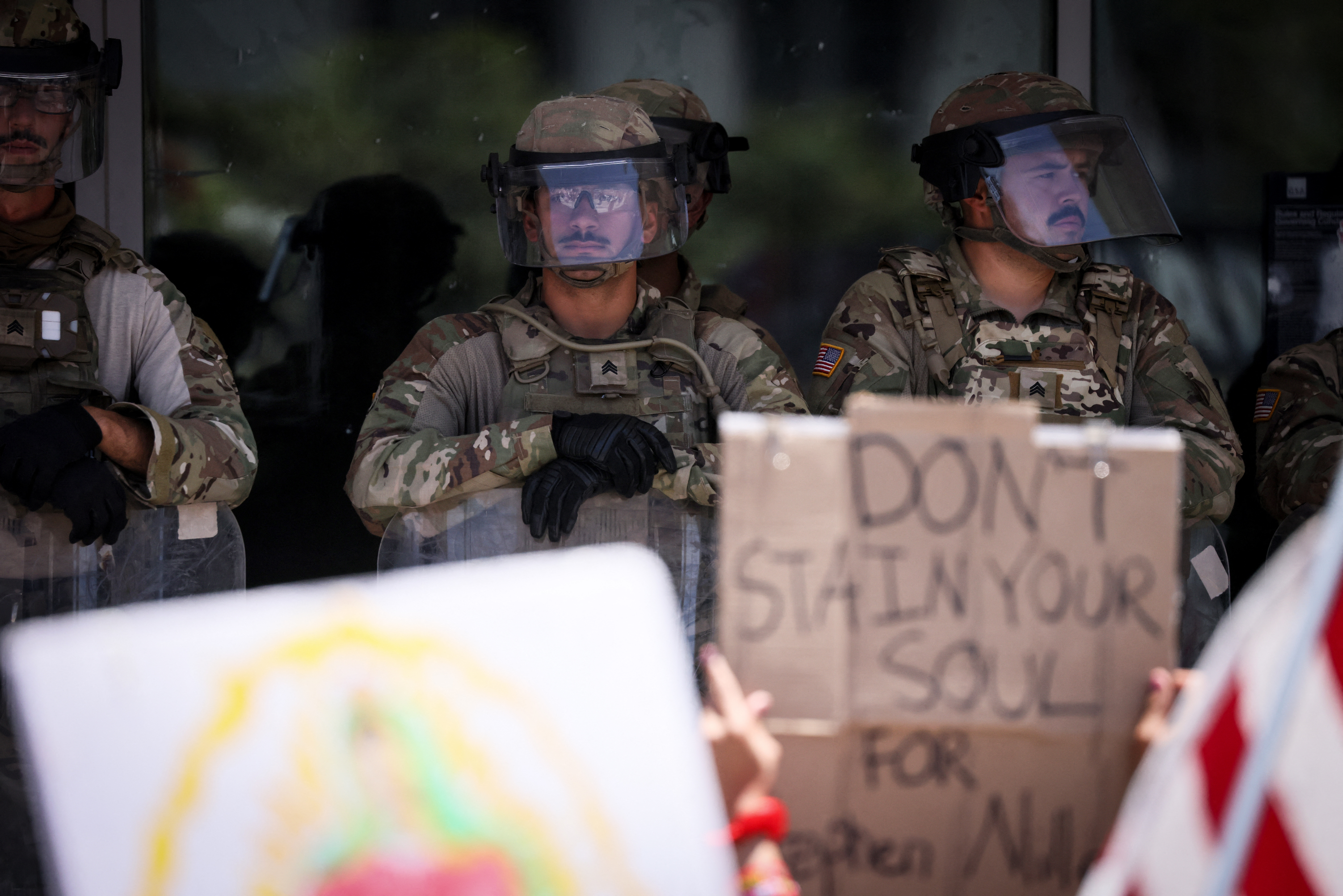 people hold protest signs in front of soldiers in riot gear