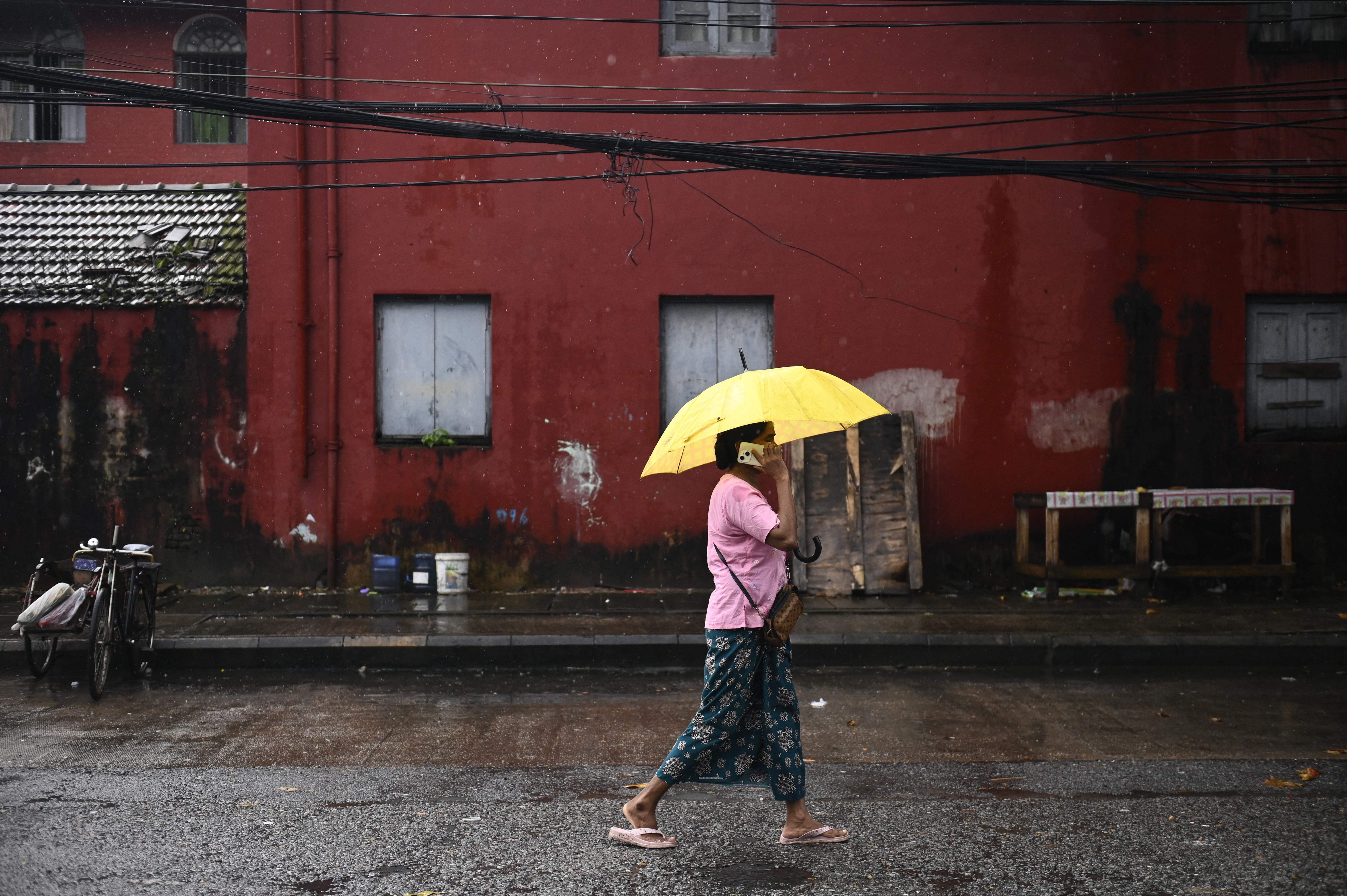 A woman talks on her mobile phone as she walks with an umbrella to shield herself from the rain in Yangon on July 16, 2025. (Photo by Sai Aung MAIN / AFP)