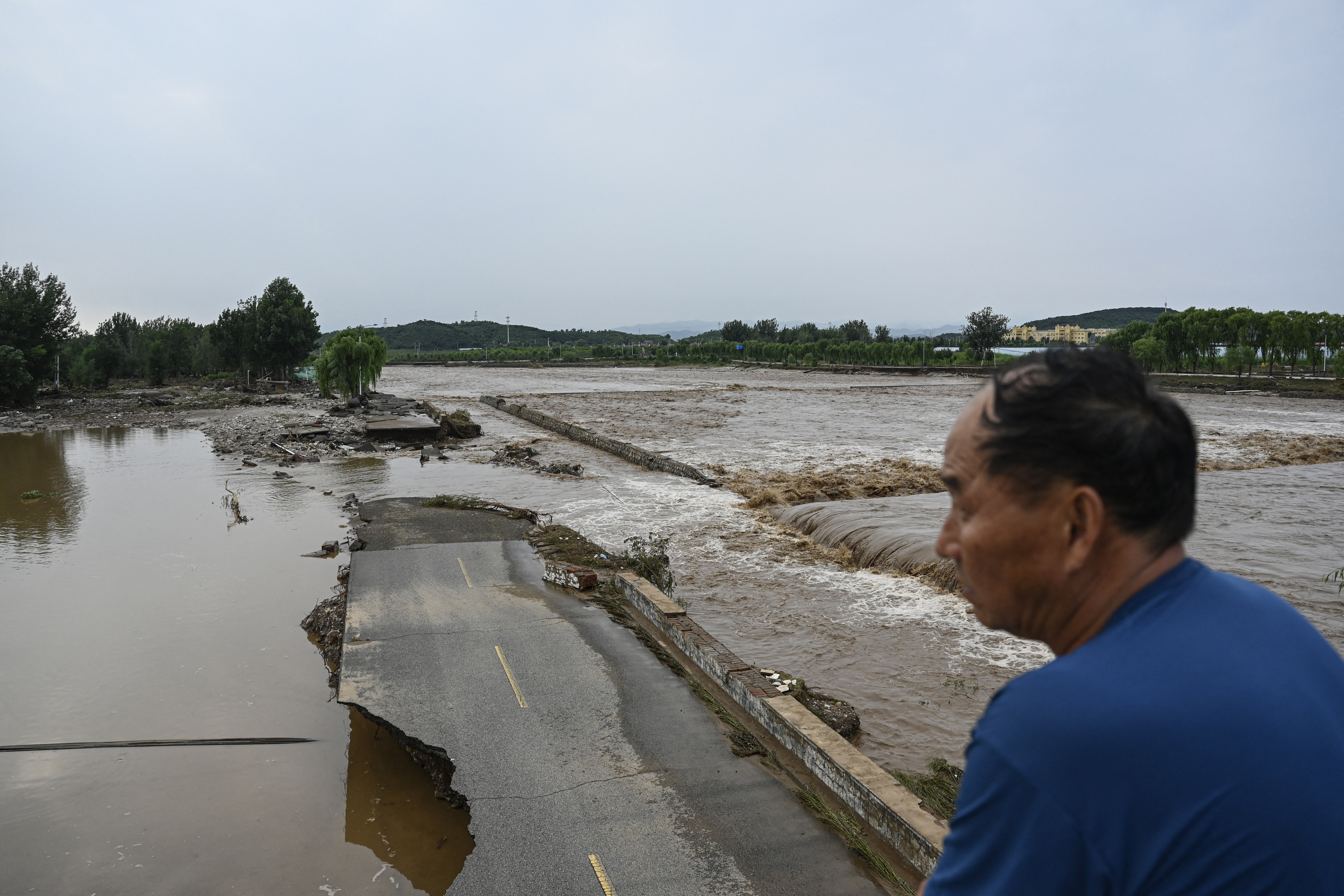 A damaged road is seen at a flooded area after heavy rains at Taishitun village in Miyun district, on the outskirts of Beijing on July 28, 2025. Torrential rain soaking northern China triggered a deadly landslide, burst riverbanks and washed away cars on July 28, with thousands of people forced to evacuate the days-long deluge. (Photo by Jade GAO / AFP)