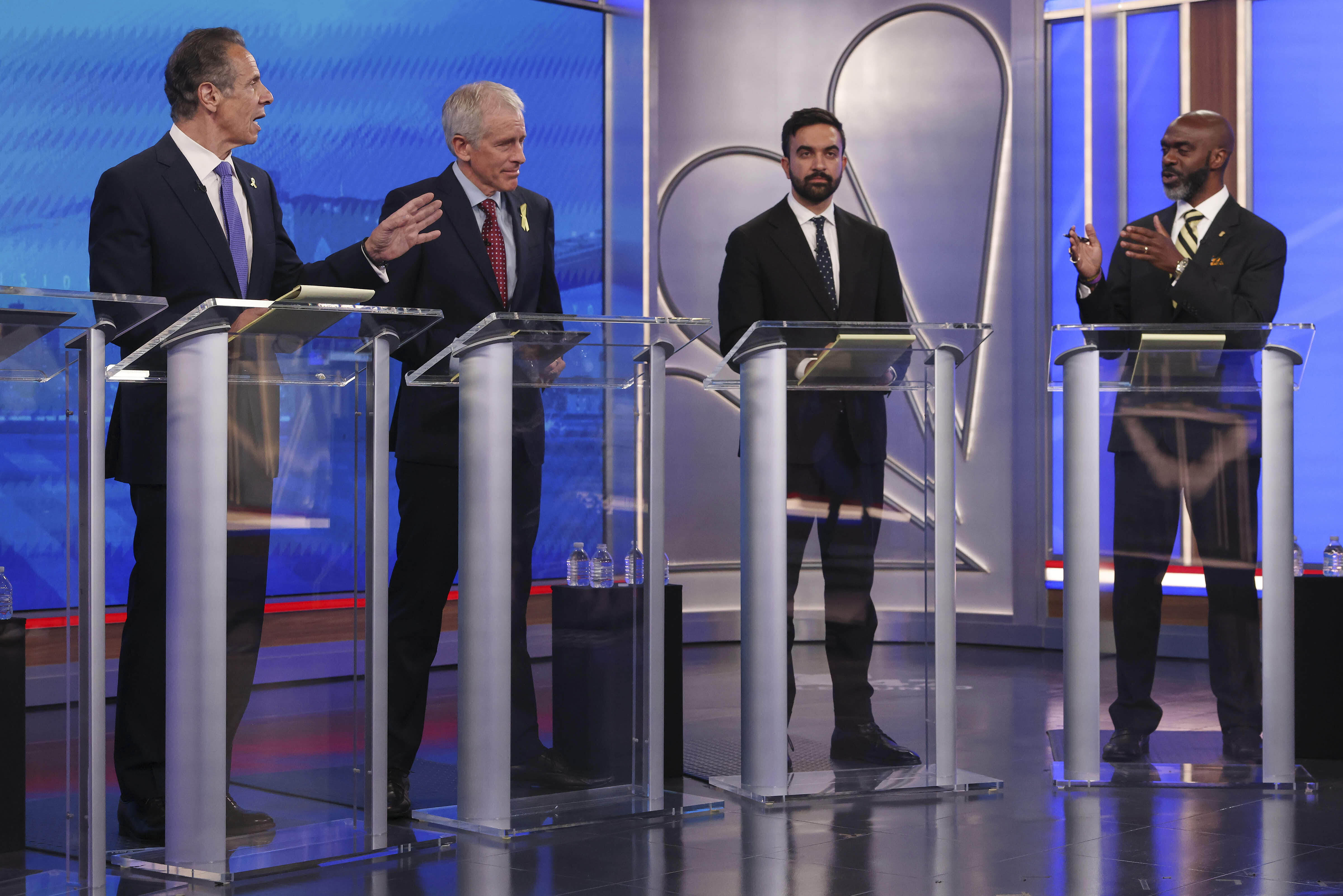 Andrew Cuomo, Michael Blake, Zohran Mamdani and Whitney Tilsen stand behind glass podiums at a debate