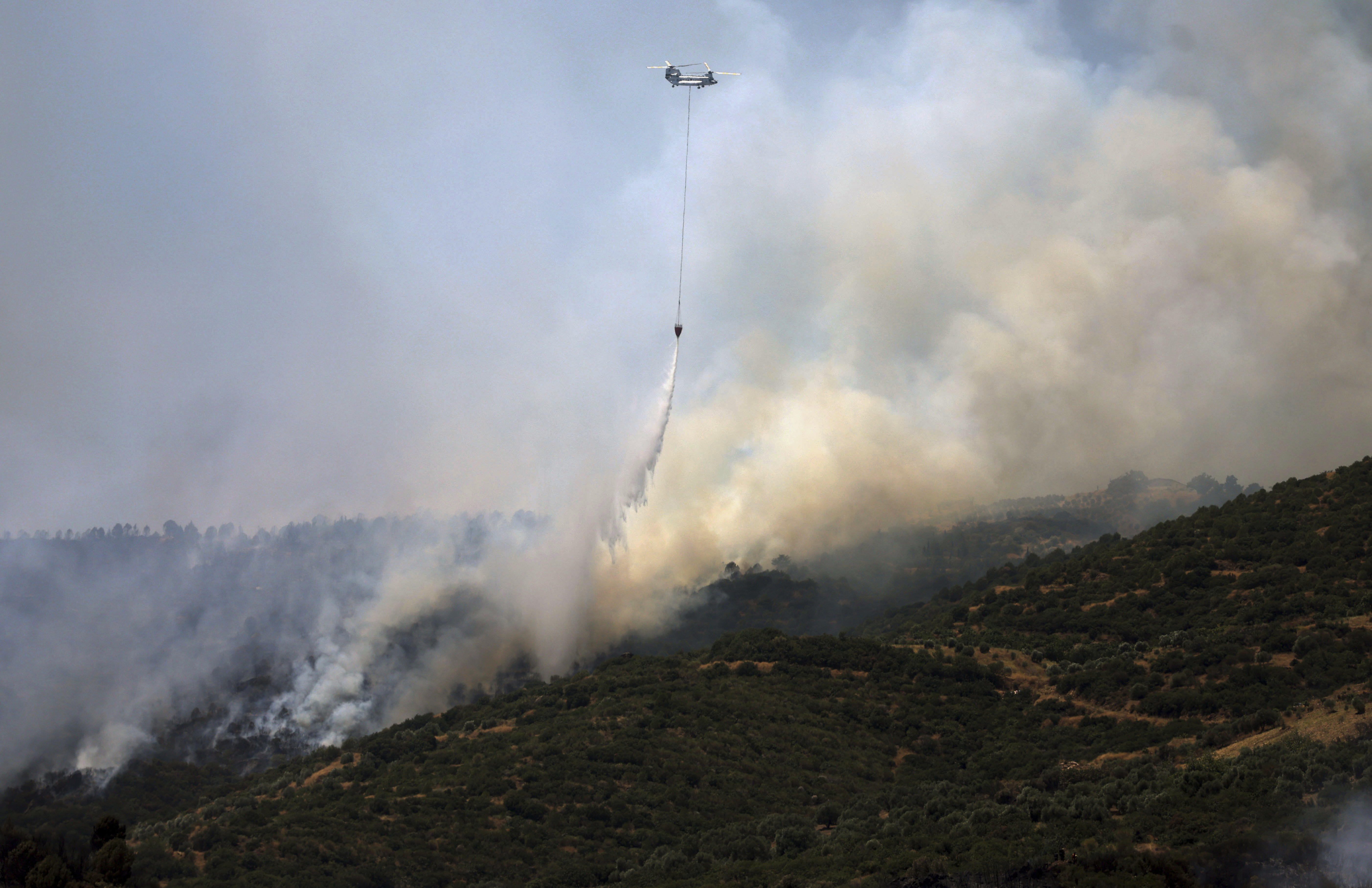 A helicopter drops water to extinguish a fire raging across a forested area.
