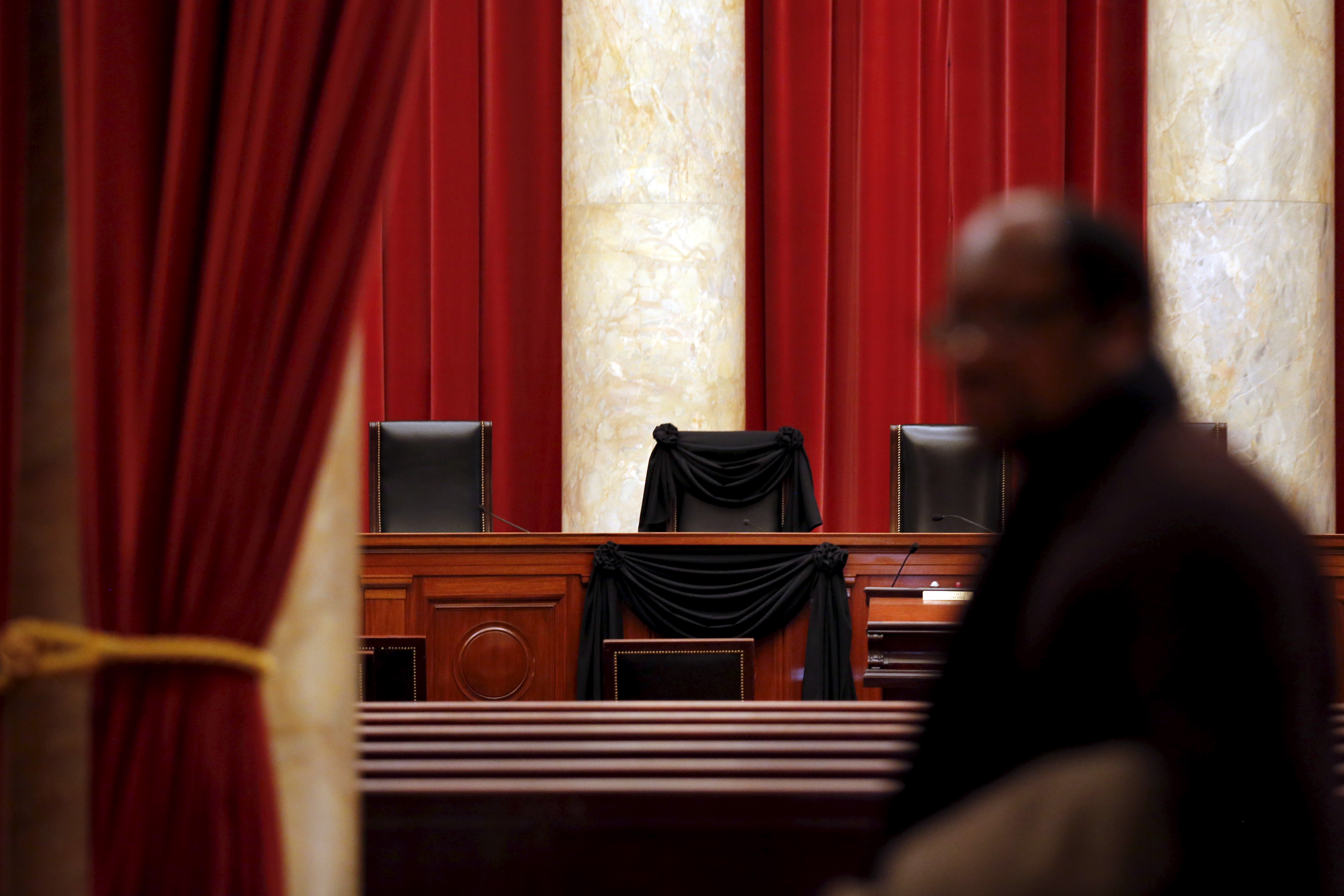 A person passes in front of the red curtains and marble columns of the Supreme Court bench.