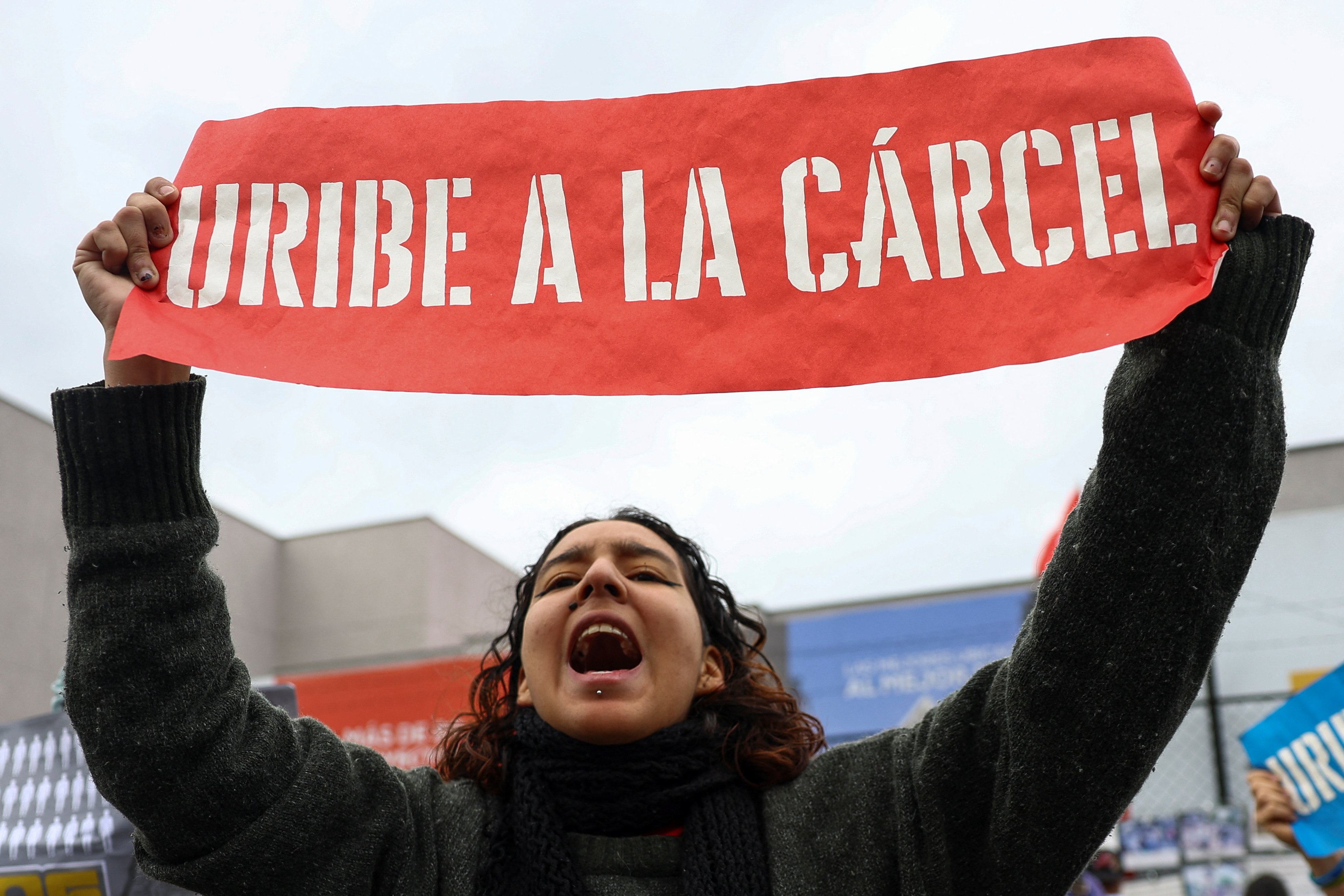 A woman holds up a banner that reads "Uribe a la Carcel."