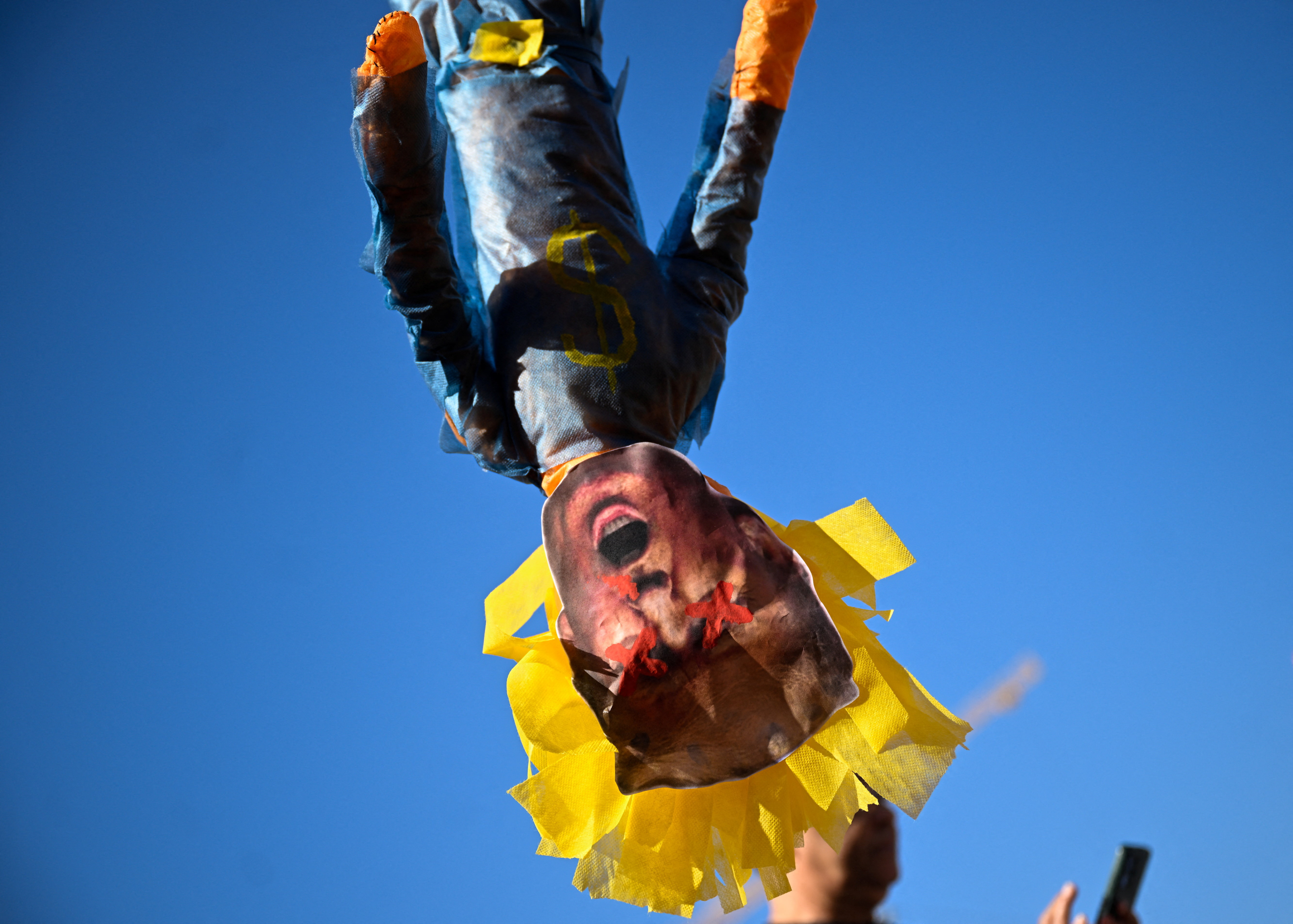 An effigy of Trump with red Xs over its eyes hangs upside down.