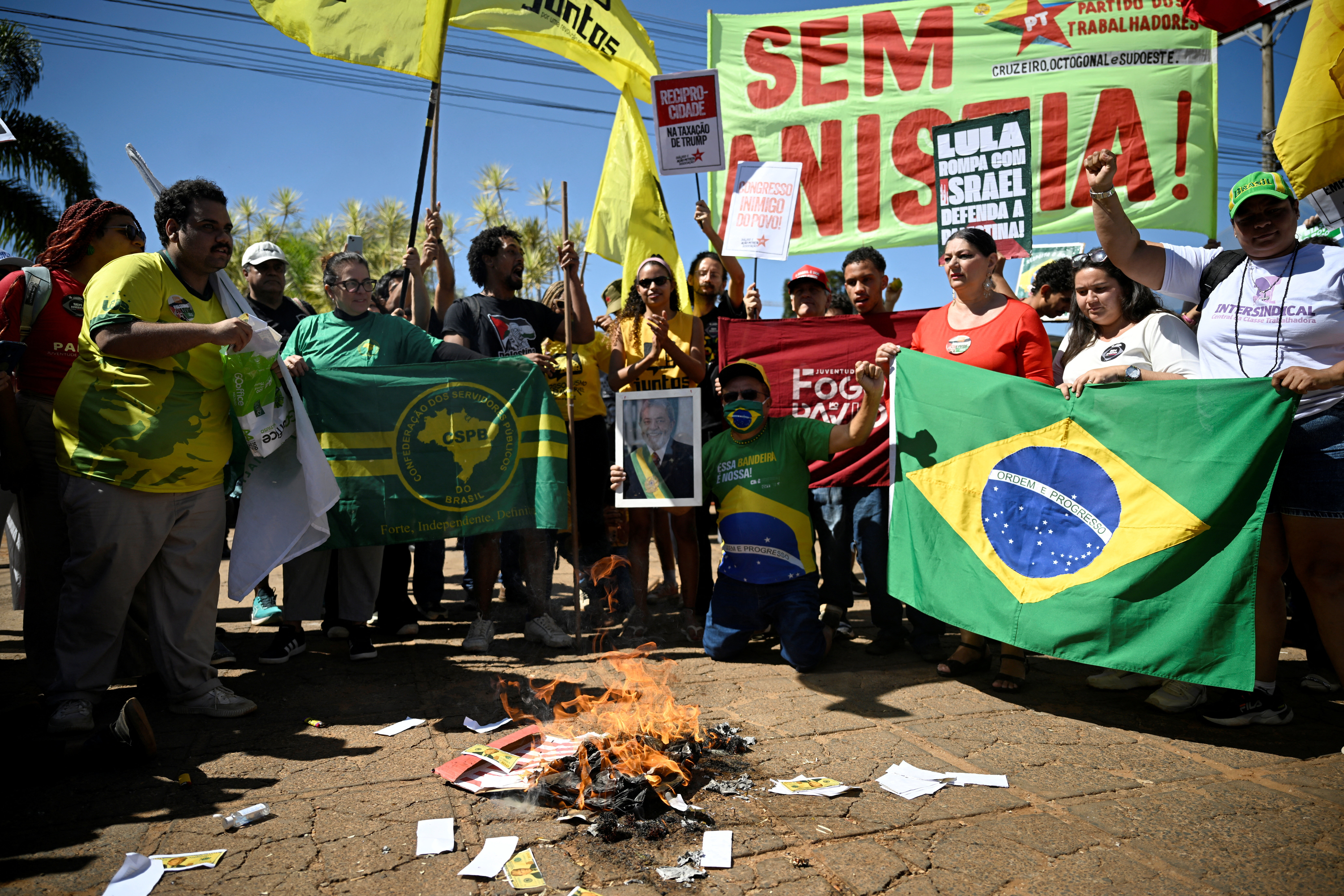 Protesters gather in a circle around a small fire that burns Trump-themed dollar bills and a US flag.