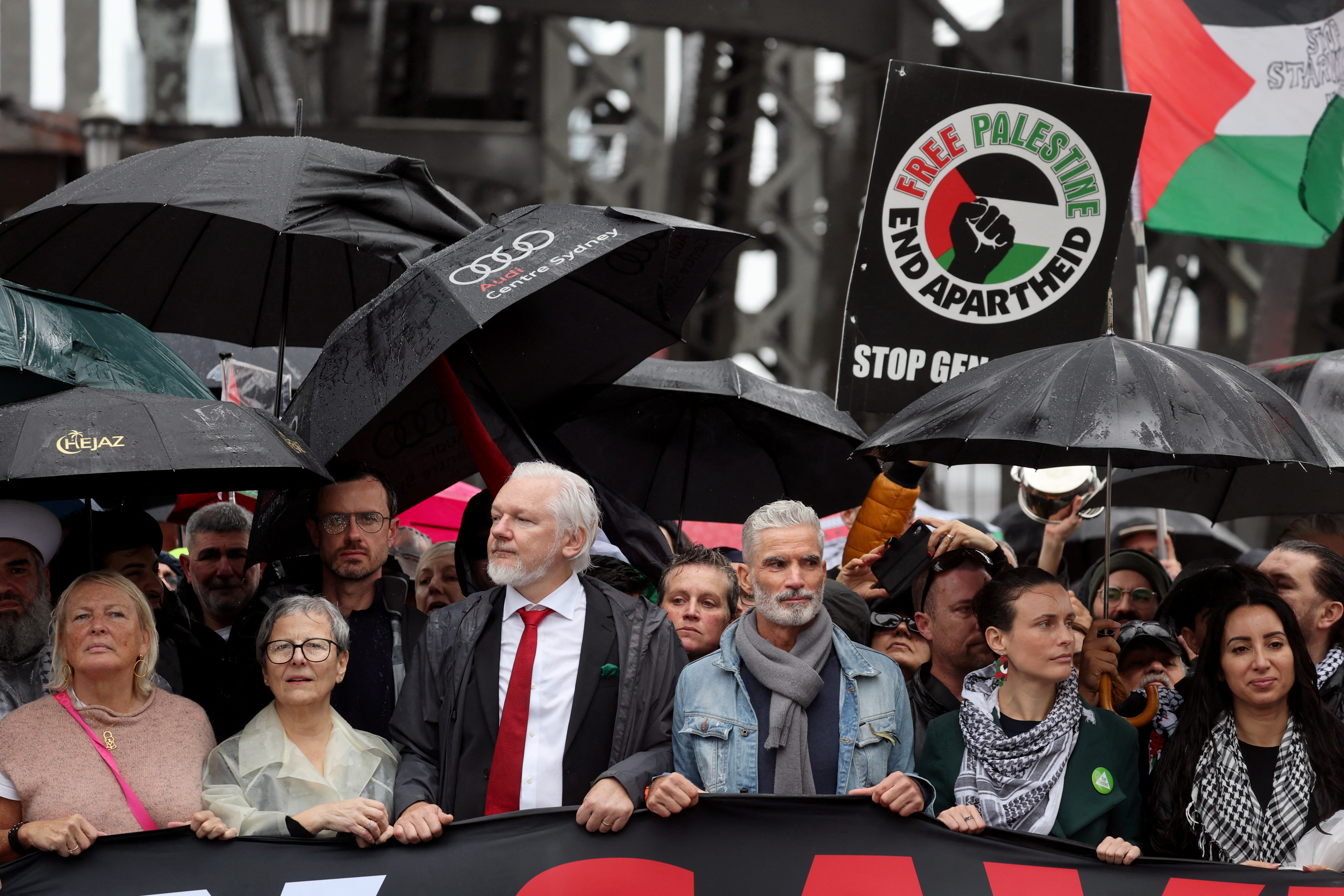 people march behind a banner that says march for humanity save gaza on a bridge