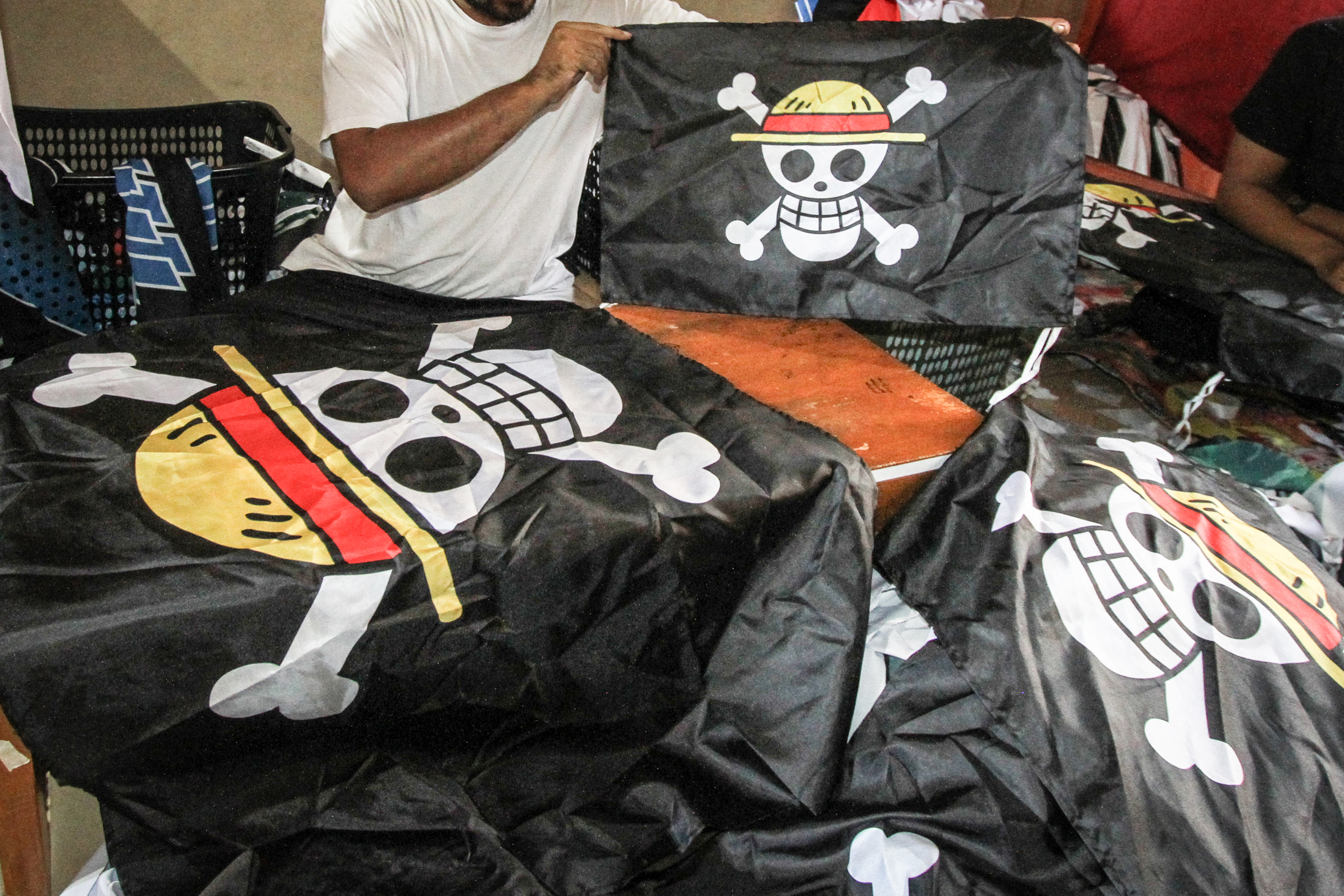 A worker holds a replica of the pirate flag from Japanese anime One Piece, made for sale as some Indonesians adopt the symbol from a story about resisting a corrupt world government to express frustration with their own, at a T-shirt workshop in Karanganyar, Central Java, on August 6, 2025, ahead of the countrys 80th Independence Day. As Indonesia's independence day approaches red and white flags will be flown across the country, but a viral anime pirate banner has drawn government threats against flying the swashbuckling ensign. A Jolly Roger skull and bone symbol topped with a straw hat from Japan's anime series 'One Piece' has caused concern among officials in Jakarta that it is being used to criticise President Prabowo Subianto's policies. (Photo by DIKA / AFP) / TO GO WITH 'INDONESIA-POLITICS-PROTEST-ANIME, FOCUS' BY DESSY SAGITA & JACK MOORE