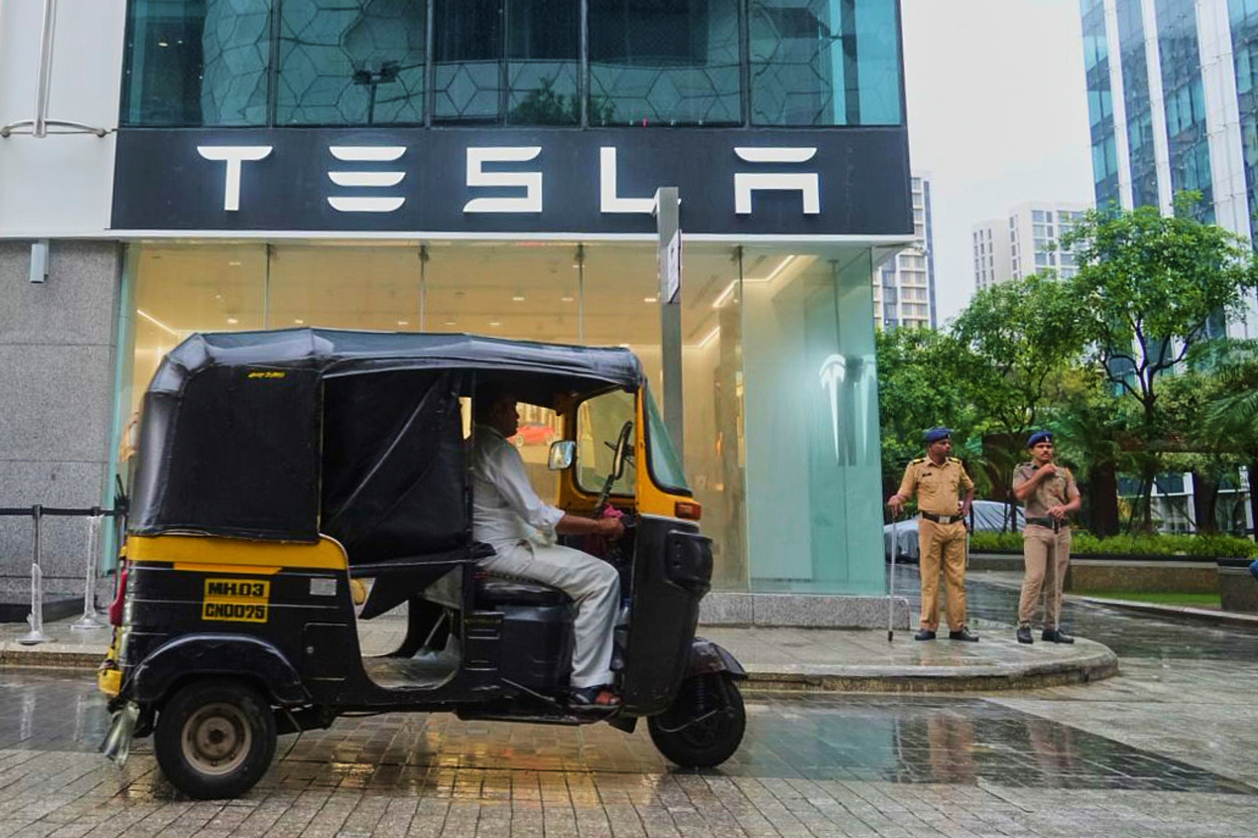Policemen stand guard as a three-wheeler auto-rickshaw drives past India's first Tesla showroom to be inaugurated in Mumbai, India
