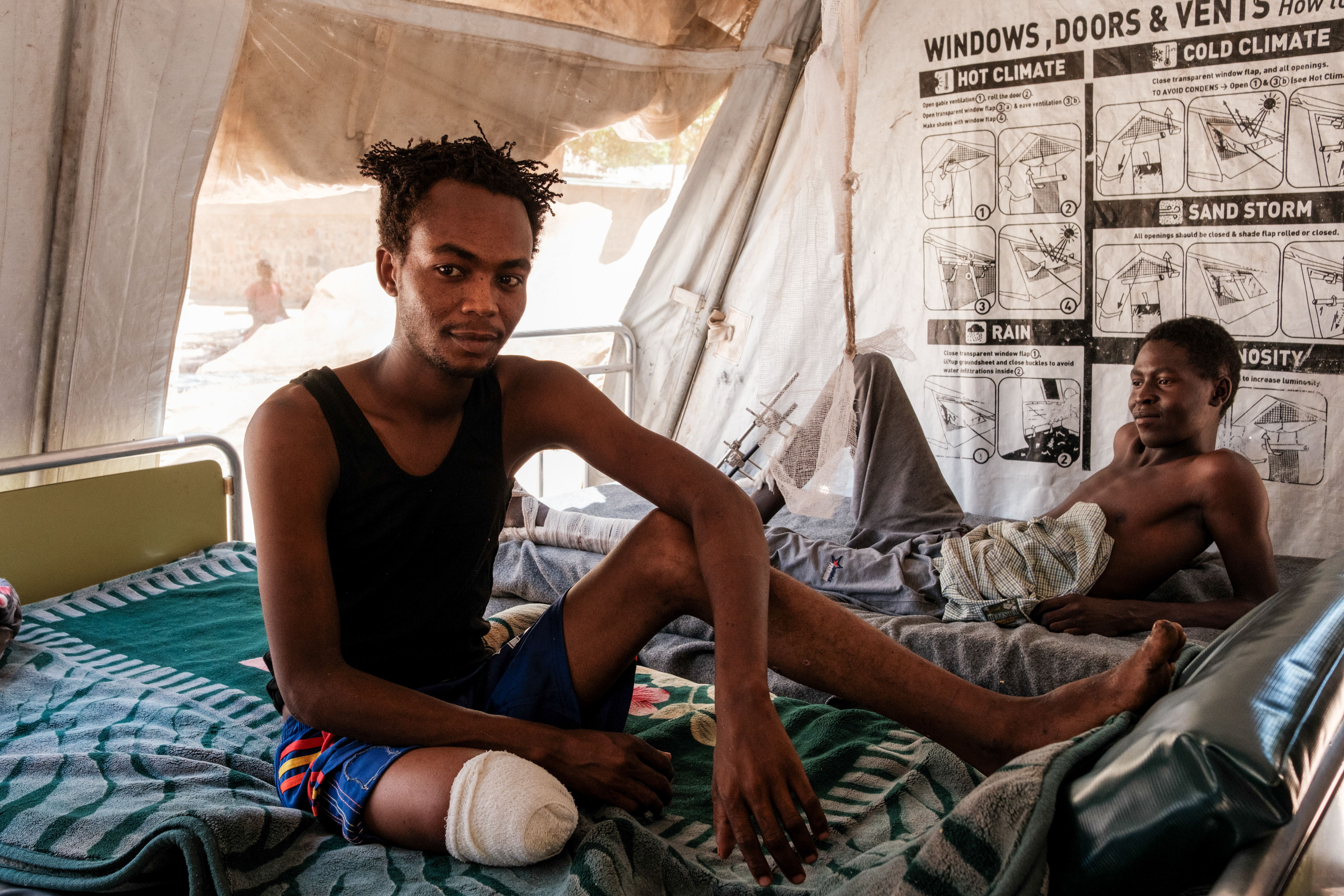 Mohamed Radi, 23, (L) a member of the Rapid Support Forces (RSF) sits on his bed with a newly amputated leg after the car he was traveling in was hit with a drone while fighting in Khor Dlib. In the back ground XXX sits with two injured legsafter setting on a landmine while fighting for the RSF at a hospital in South Kordofan on April 21, 2025
