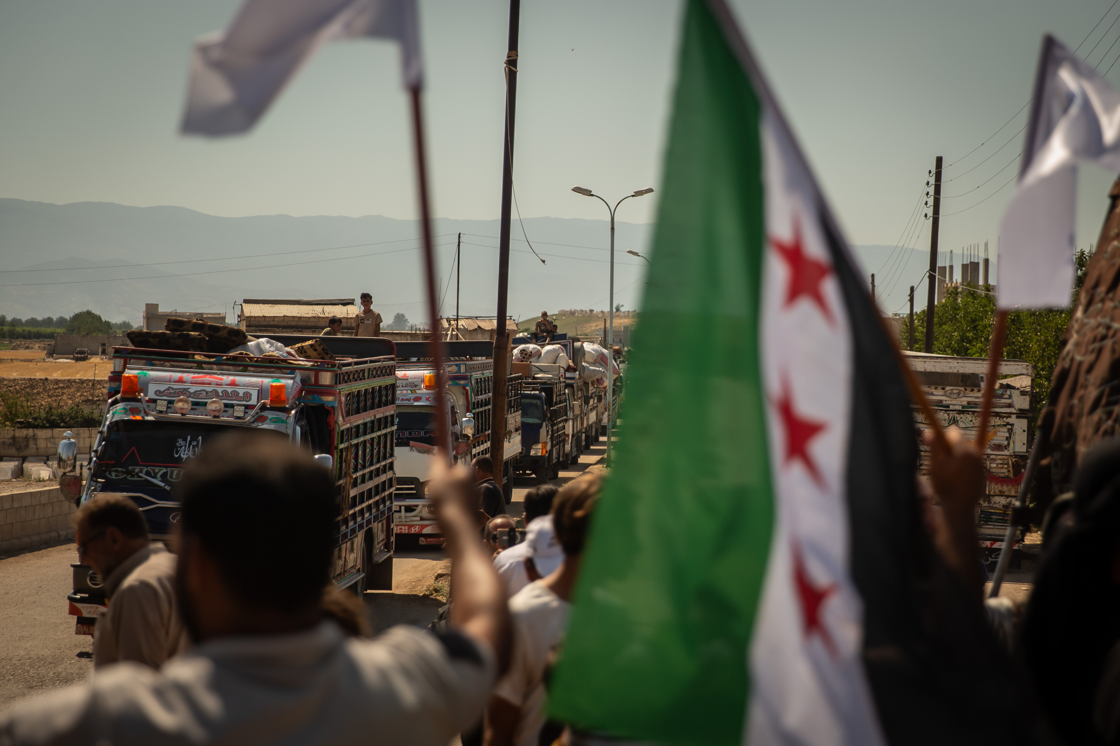 A Syrian flag in the foreground with trucks visible in the background
