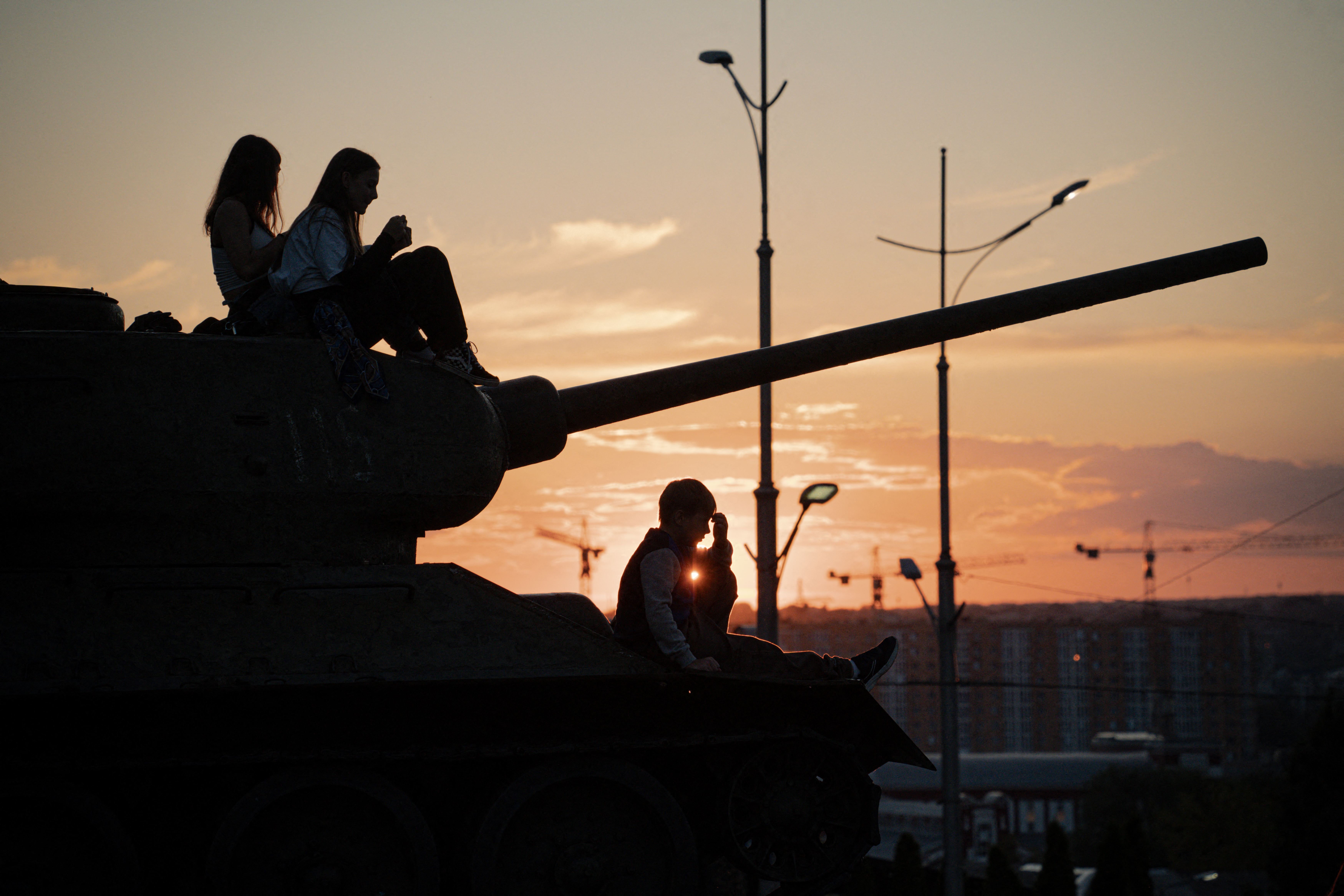A silhouette can be seen of people sitting on a tank at dusk