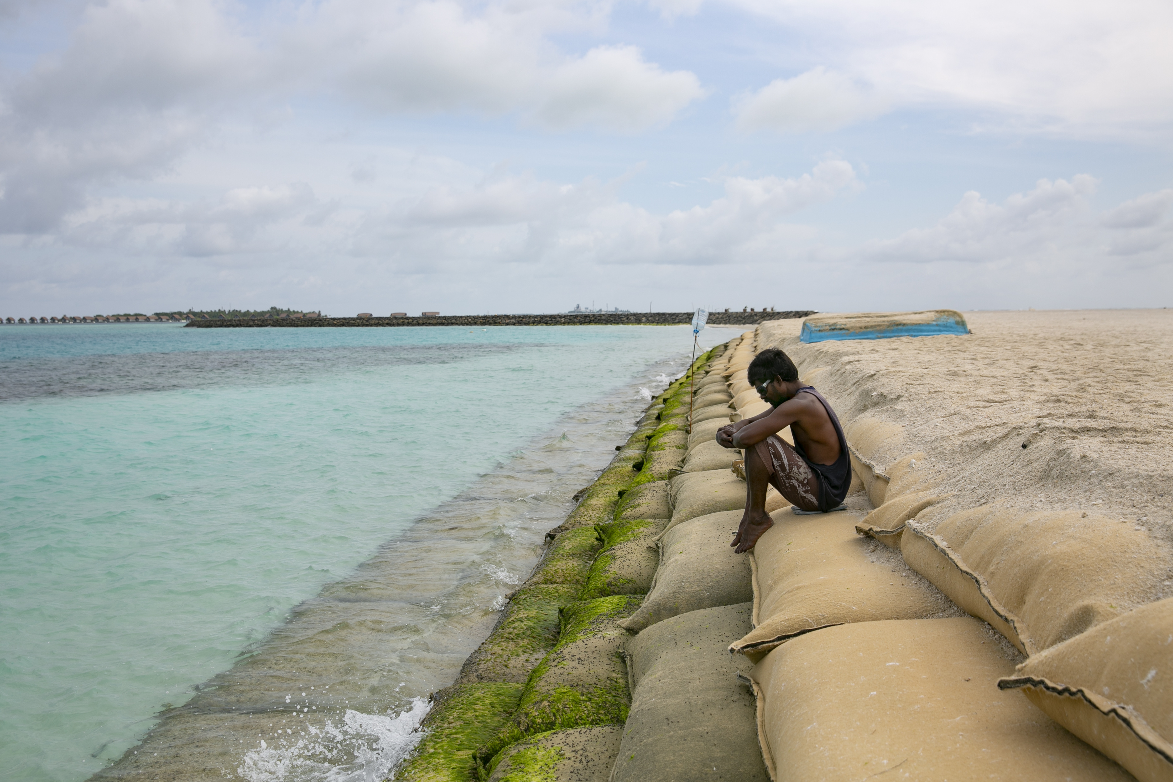 GURAIDHOO, MALDIVES - OCTOBER 10: A man sits on a protective sand bag wall on October 10, 2021 in Guraidhoo, Maldives. The Maldives is one of the world's lowest-lying countries; more than 80% of Maldives land is less than one meter above sea levels, making it extremely vulnerable to climate change. At current global warming rates, 80% of the Maldives could be submerged by 2050. At the recent UN General Assembly, when discussing the threat of climate change, Maldives President Ibrahim Mohamed Solih said, "There is no guarantee of survival for any one nation in a world where the Maldives cease to exist." (Photo by Allison Joyce/Getty Images)