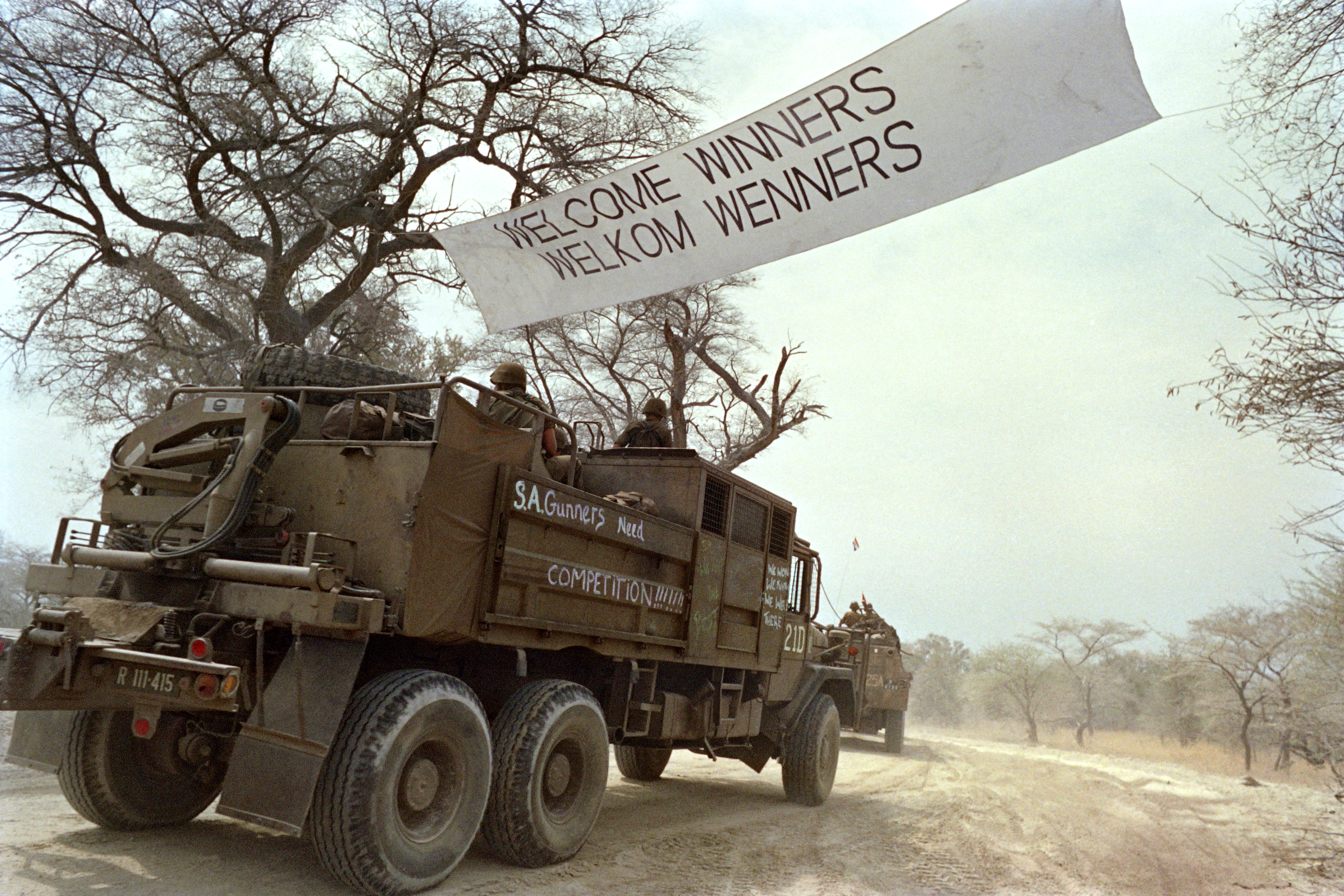 Military forces cross a border under a banner saying 'Welcome Winners'.