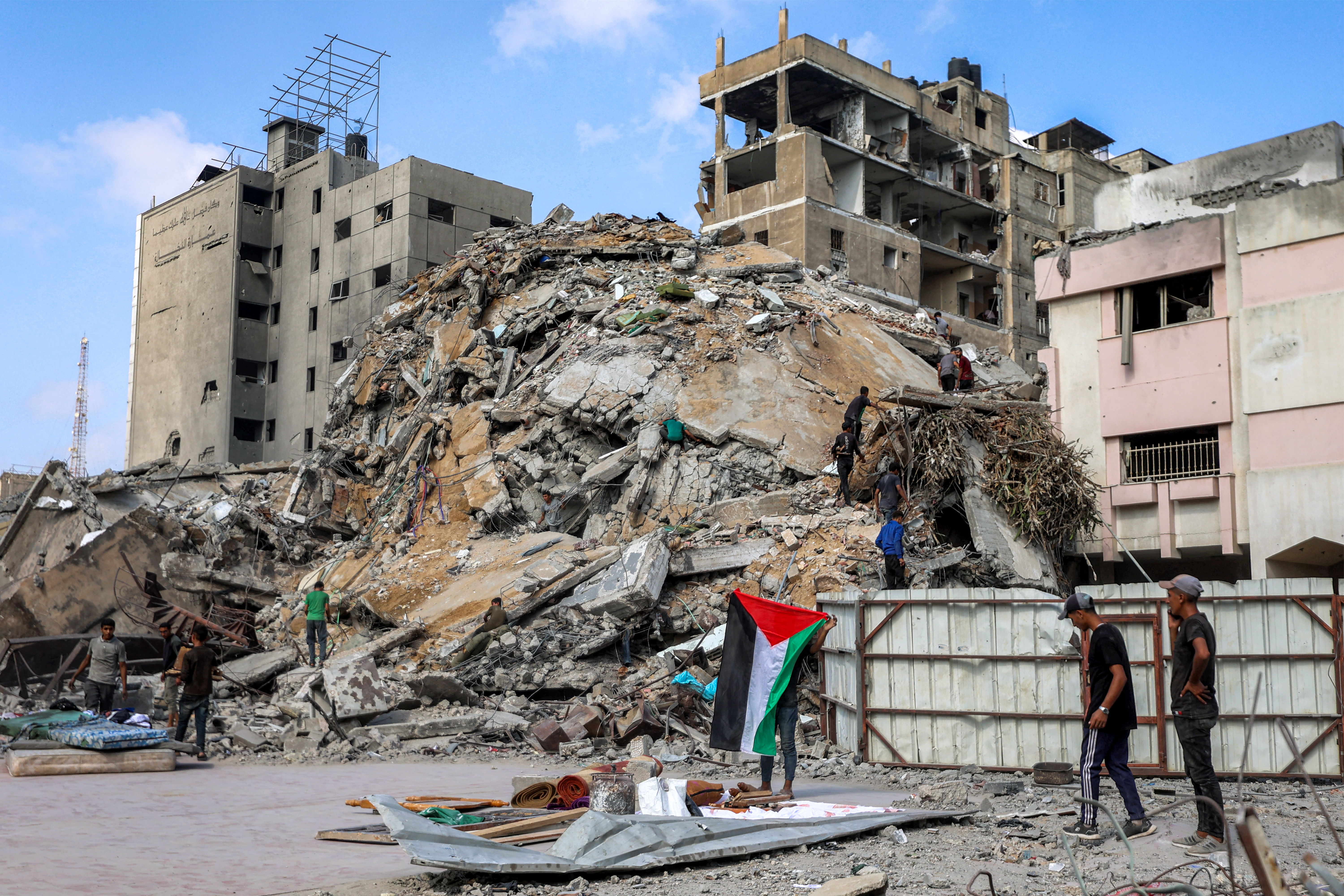 A boy unfurls a Palestinian flag as people inspect for salvage the rubble of the Unknown Soldier Tower, after it was destroyed by overnight Israeli bombardment, in the Rimal neighbourhood of Gaza City on September 15, 2025.