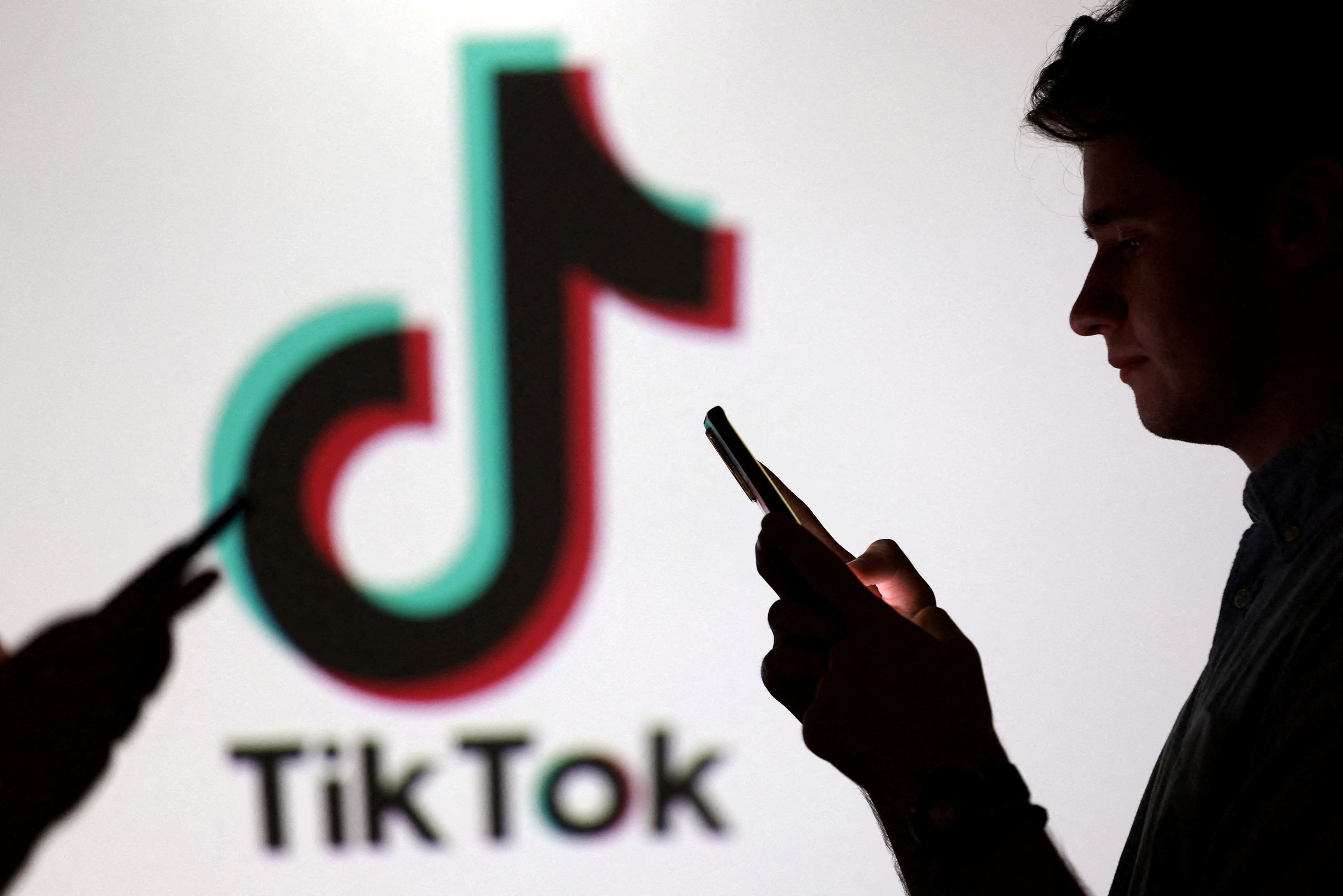 FILE PHOTO: Teenagers pose for a photo while holding smartphones in front of a TikTok logo in this illustration taken September 11, 2025. REUTERS/Dado Ruvic/Illustration/File Photo