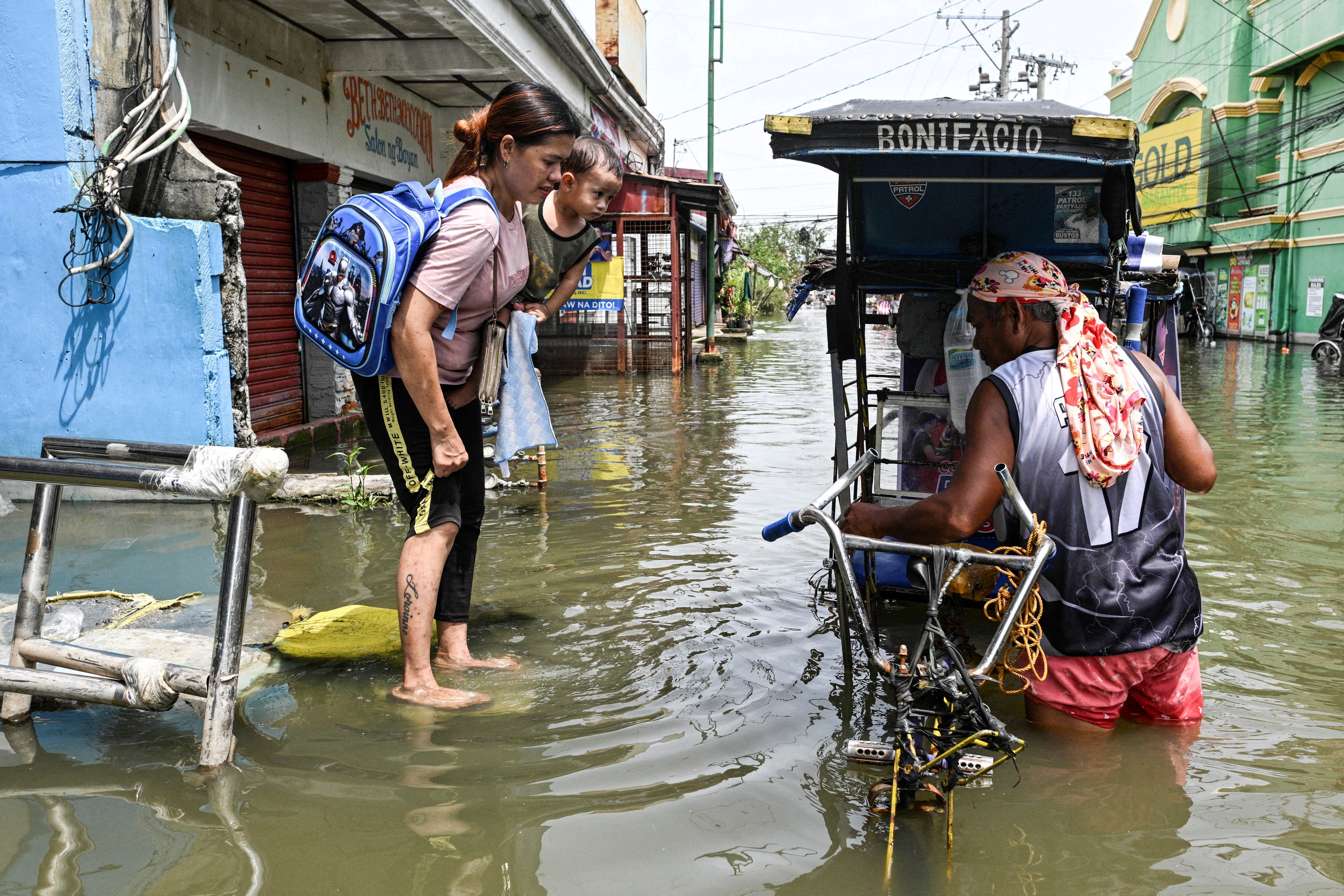 A woman carrying a baby prepares to ride a pedicab to cross a flooded street in San Roque, Macabebe, Pampanga, Philippines