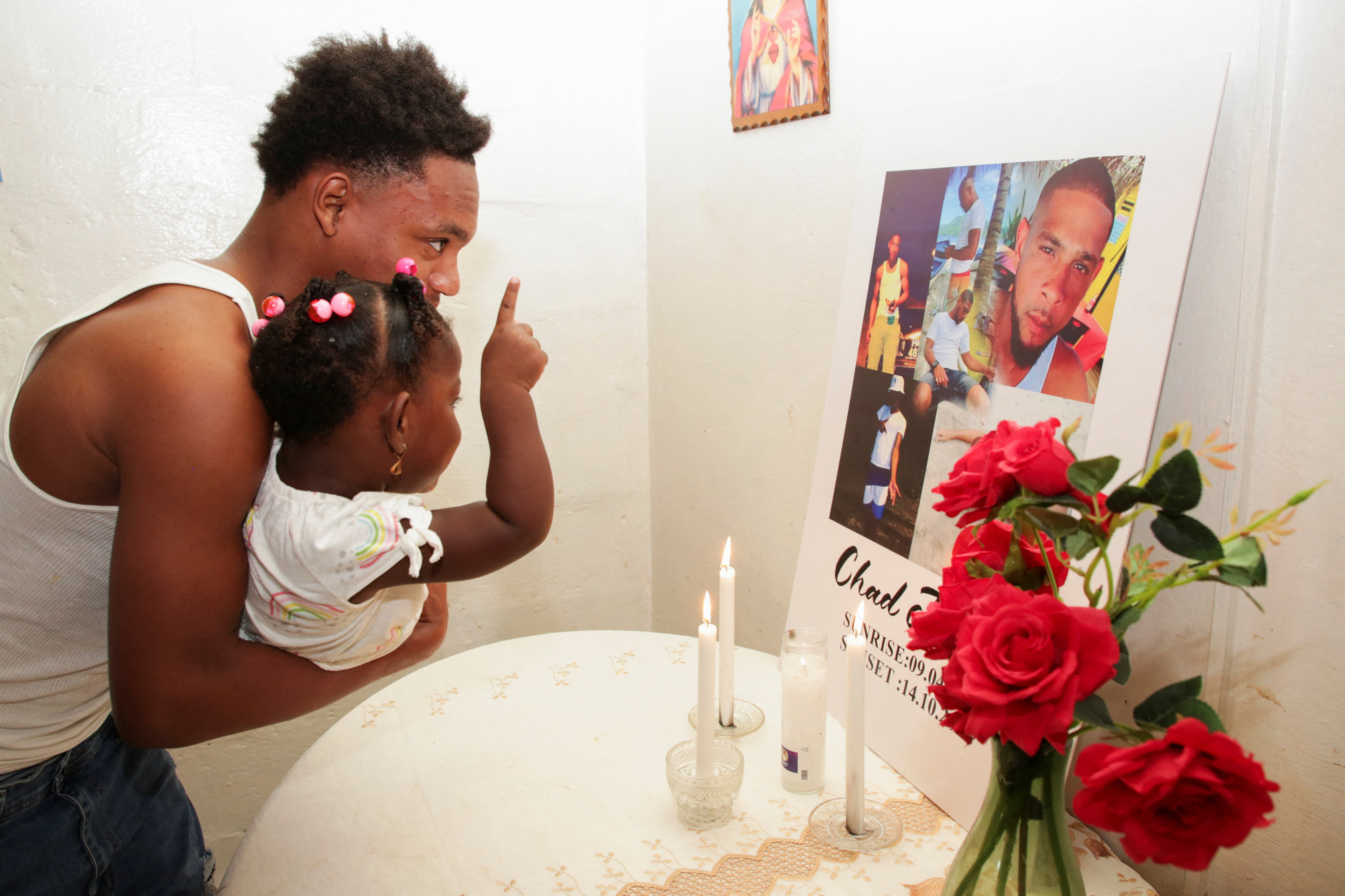 A man holding a toddler looks at a memorial photo