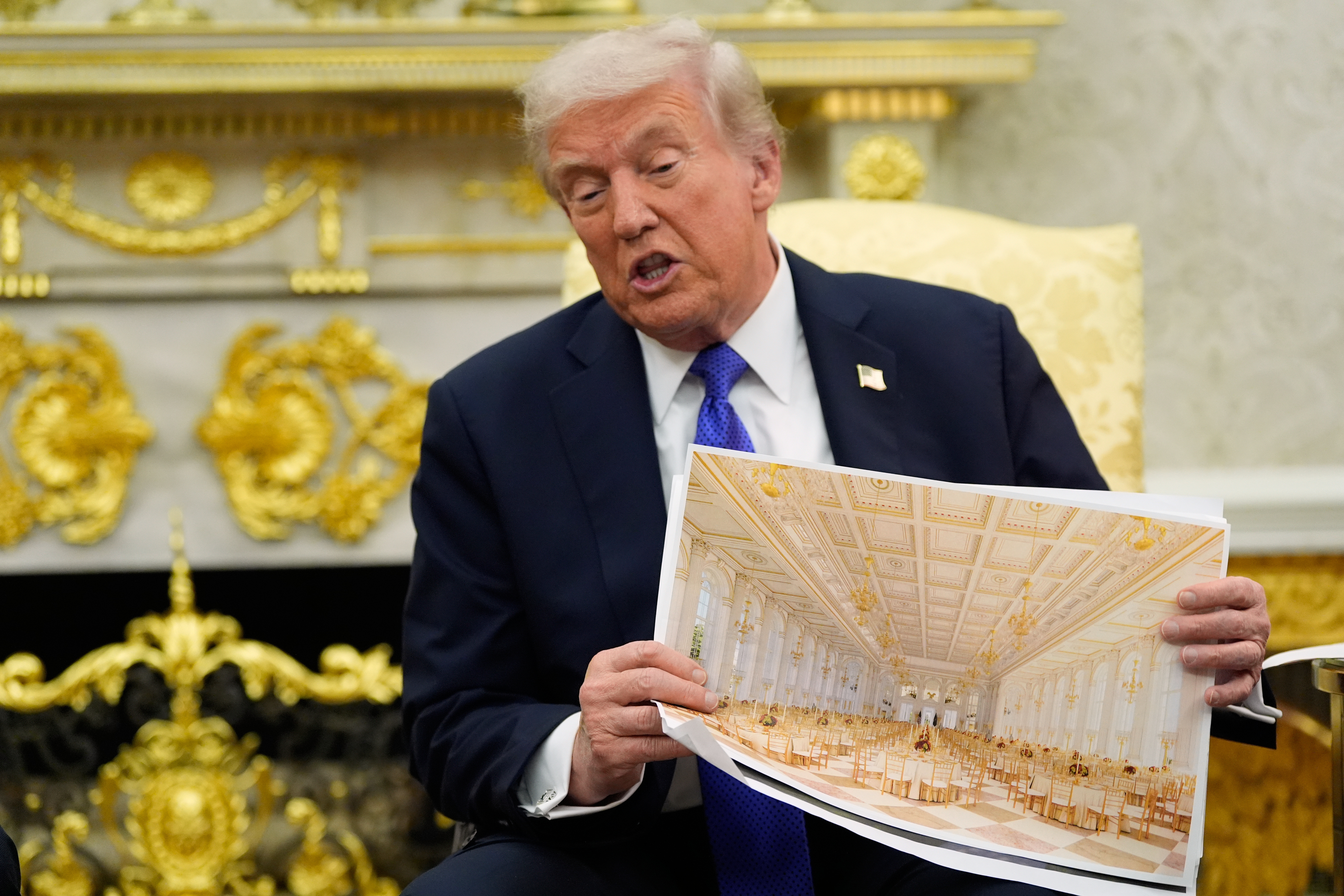 Donald Trump holds up plans for his White House ballroom in the Oval Office.
