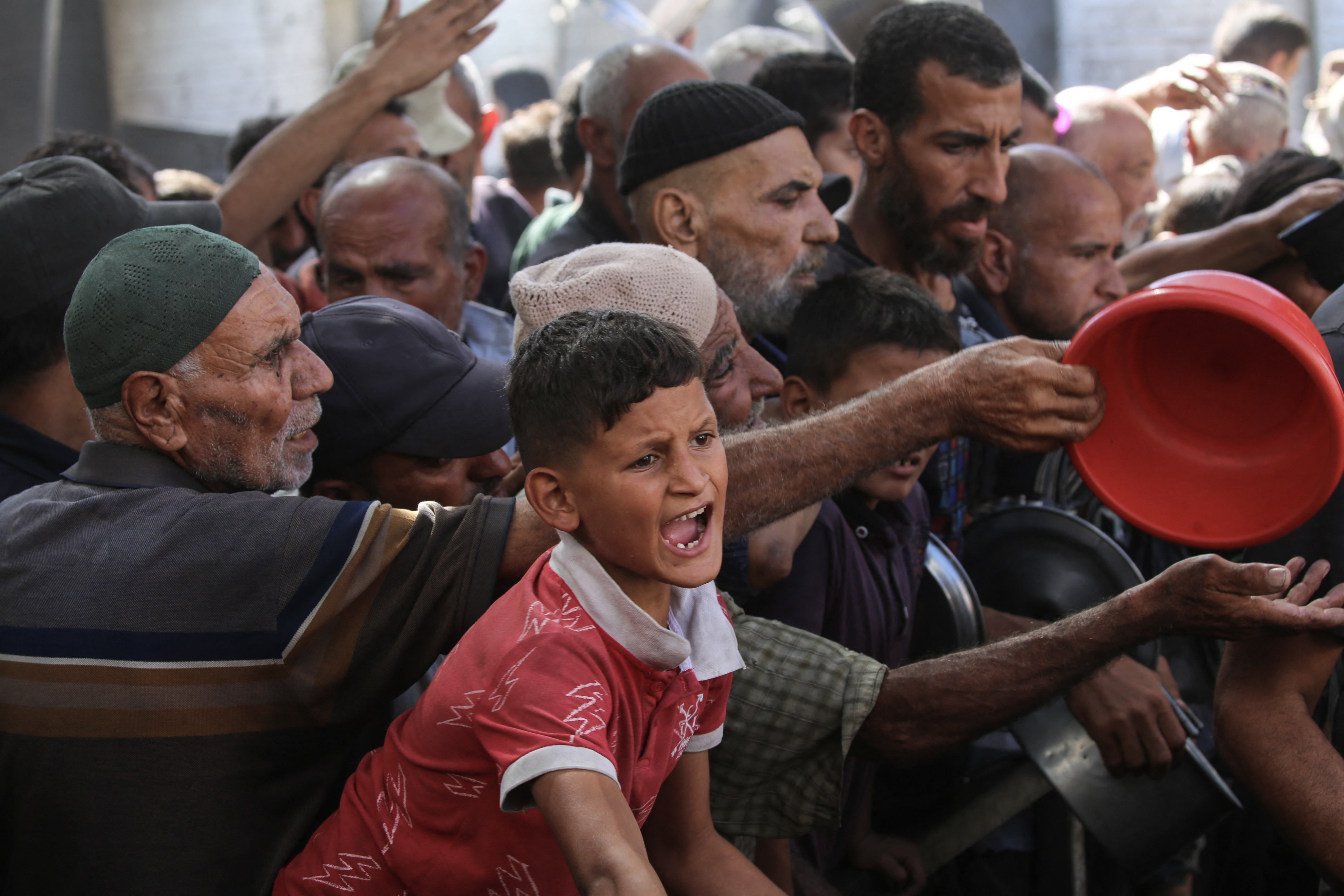 A boy reacts as Palestinians gather to receive food portions from a charity kitchen in the Nuseirat refugee camp, located in the central Gaza Strip, on October 15, 2025, two days after a ceasefire came into effect.