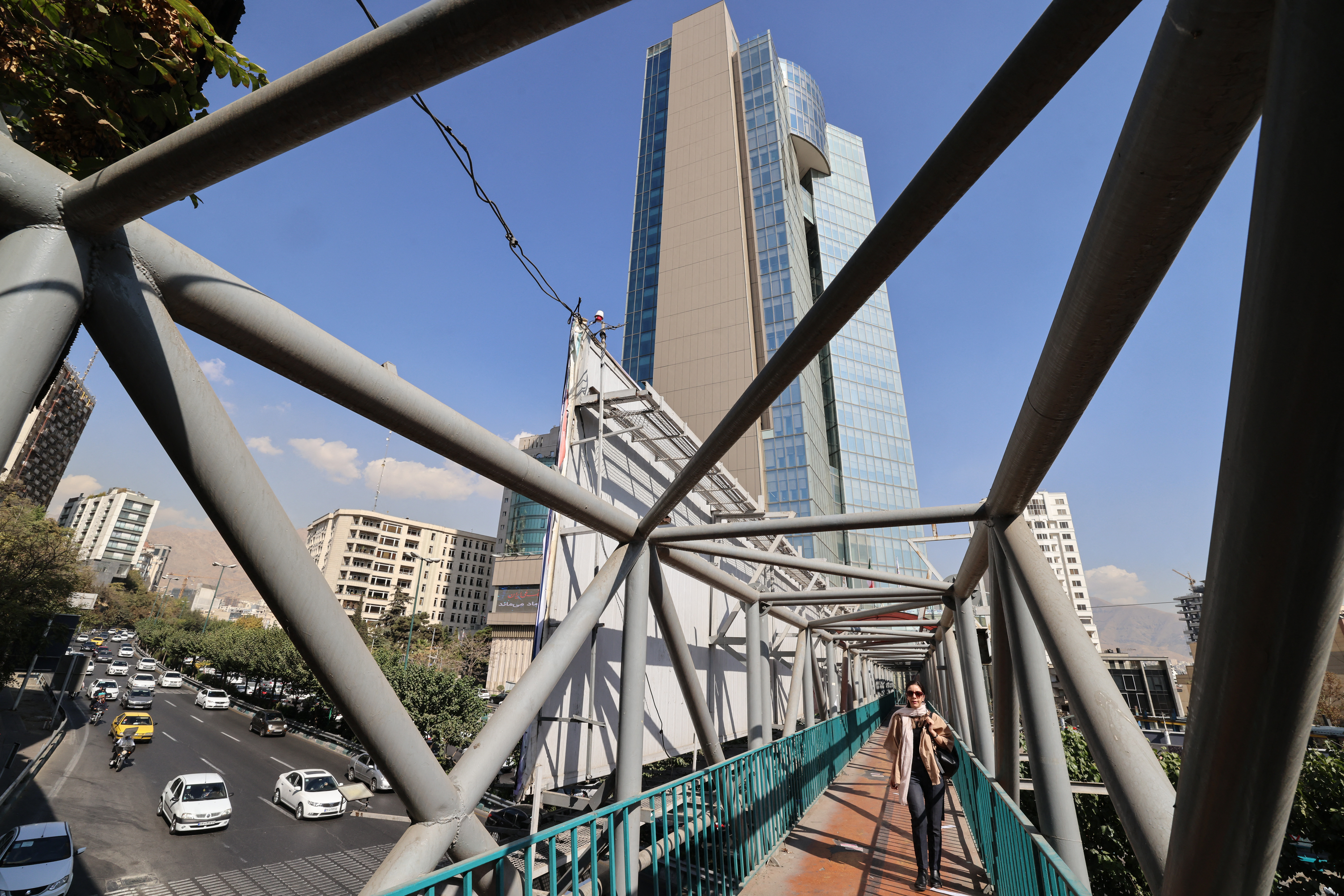 An Iranian woman walks beneath the former headquarters of the now-defunct Ayandeh Bank in the capital Tehran on October 25, 2025.