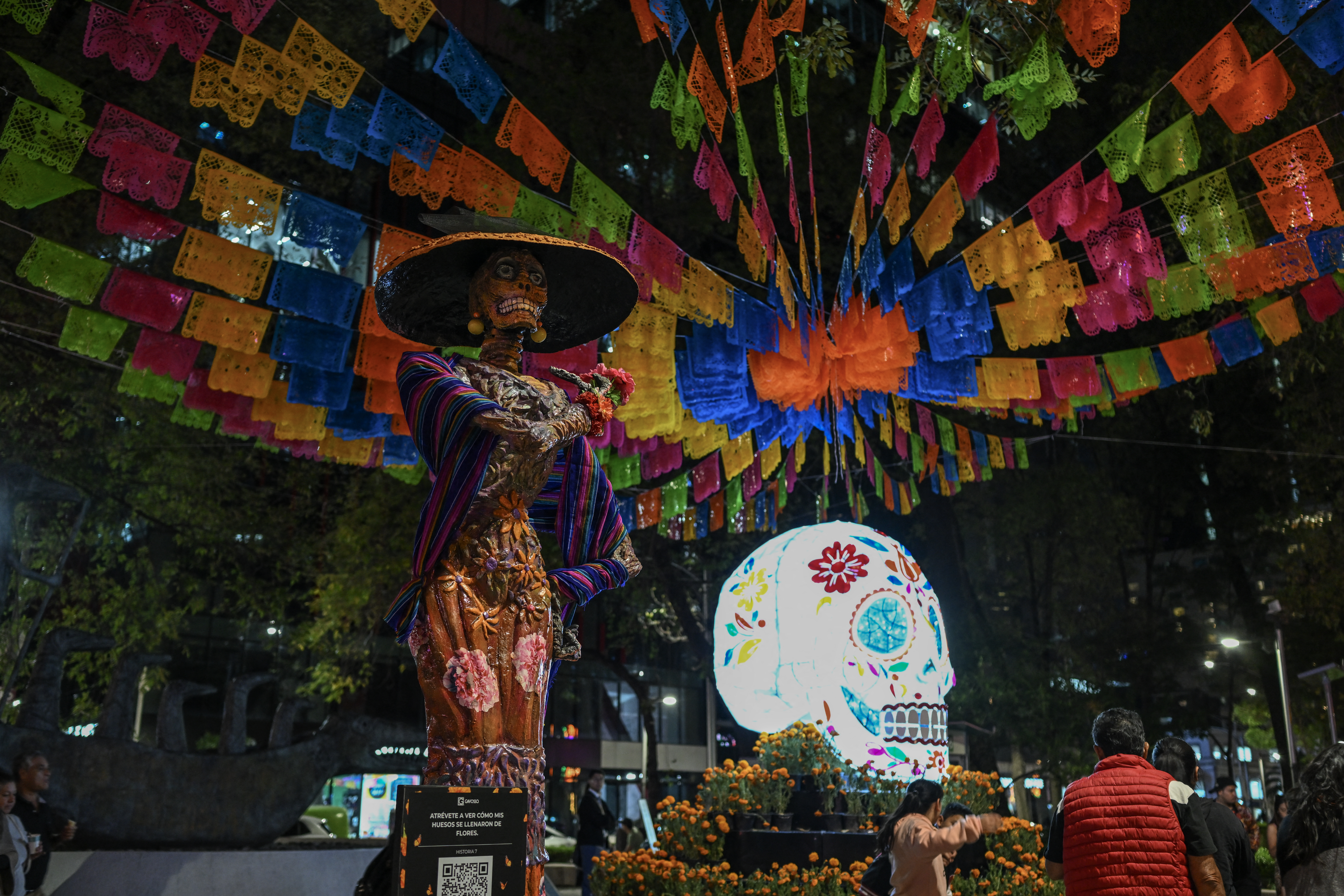 Pedestrians and tourists walk past an illuminated Catrina during the International Festival of Lights as part of the Day of the Dead celebrations in Mexico City on October 27, 2025.