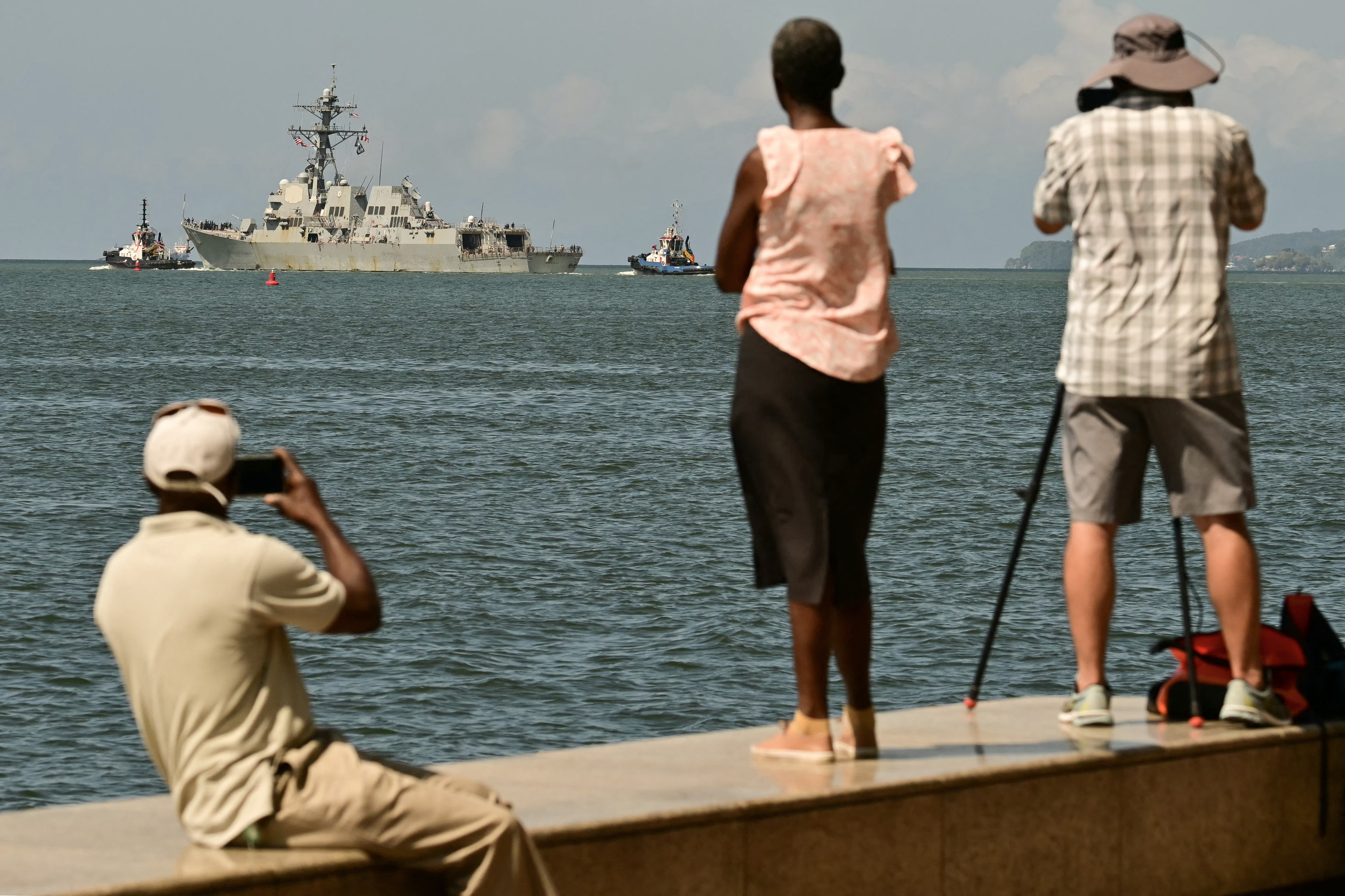 TOPSHOT - People watch and take pictures of the USS Gravely, a US Navy warship, departing the Port of Port of Spain on October 30, 2025.