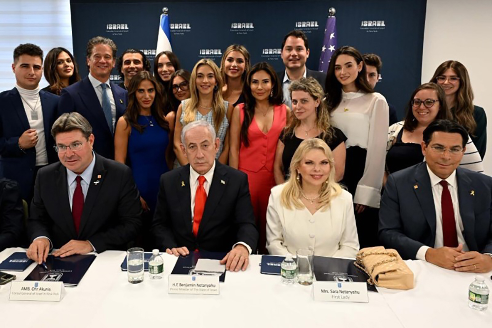 Israeli PM Benjamin Netanyahu seated and accompanied by his wife Sara Netanyahu and foreign minister Danny Danon, while pro-Israel social media influencers stand behind them