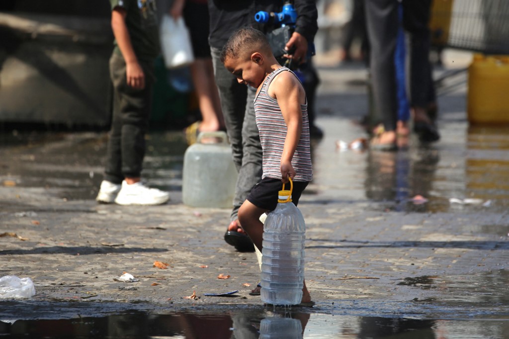 A Palestinian boy carries a large plastic bottle filled with water at a displacement camp.
