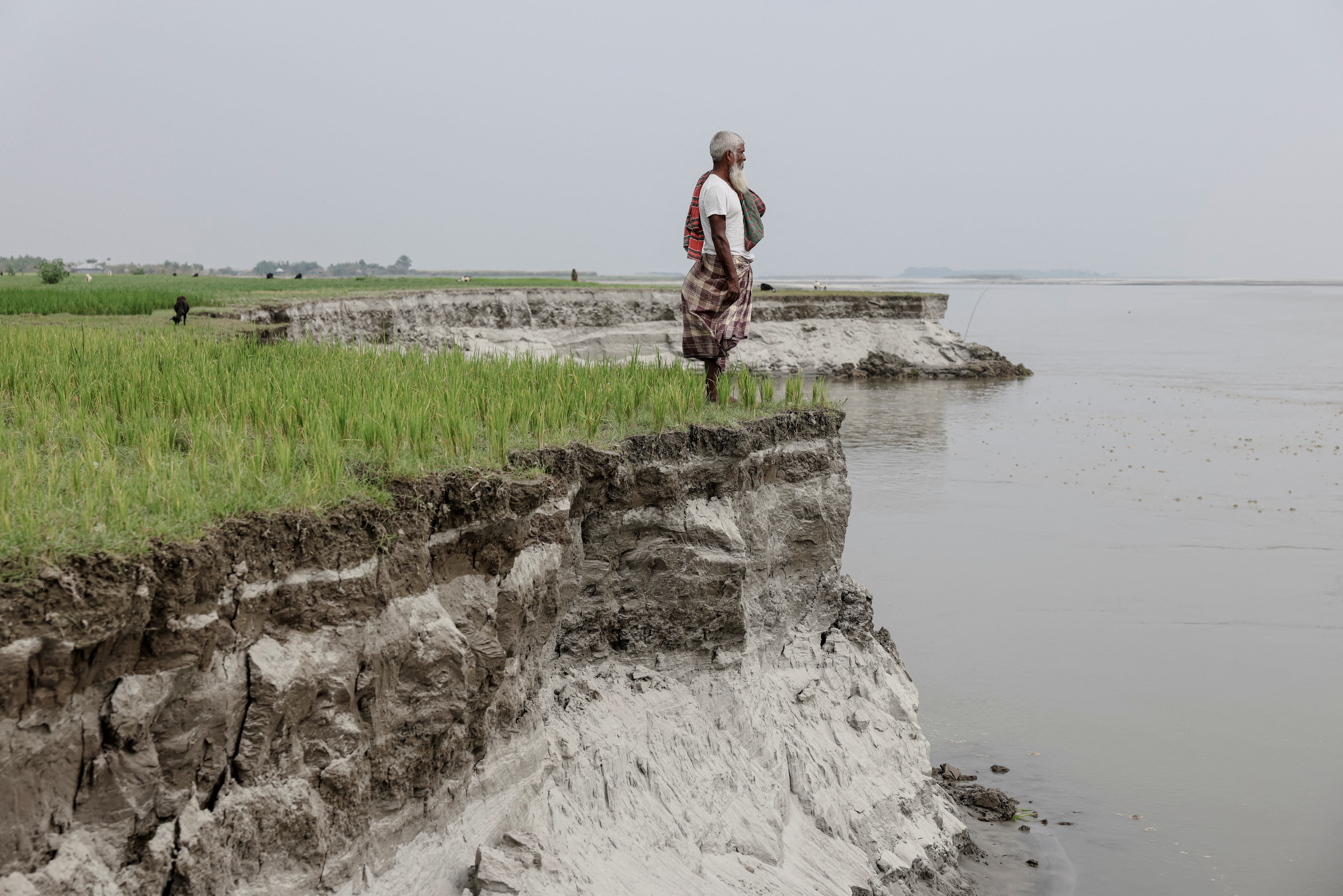 Kosim Uddin, 50, looks toward the site of his vanished home as he poses for a picture on an island in the Brahmaputra River, where he recently relocated due to erosion, in Kurigram, Bangladesh