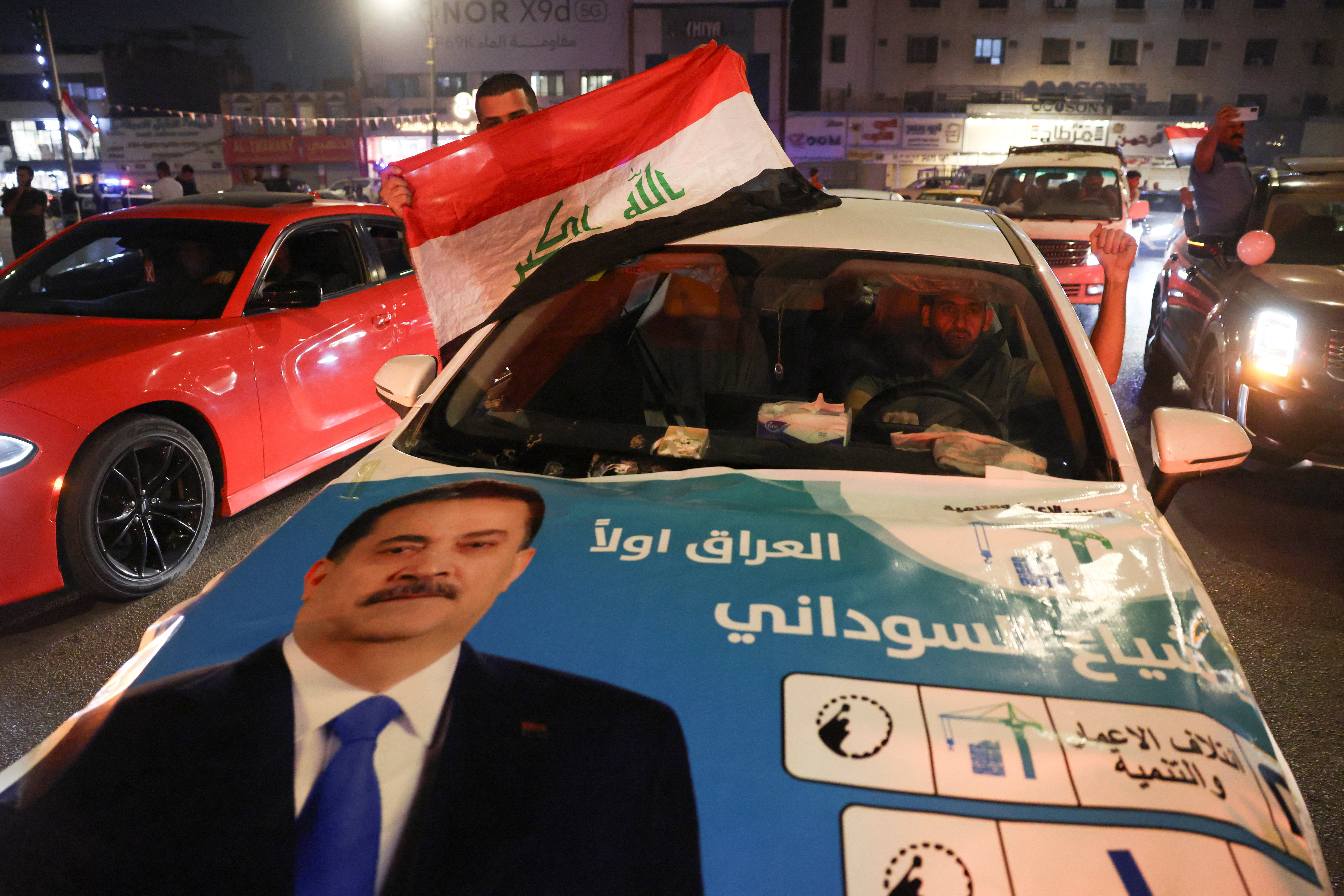A man holds an Iraqi flag from a car with an election poster featuring incumbent Prime Minister Mohammed Shia al-Sudani