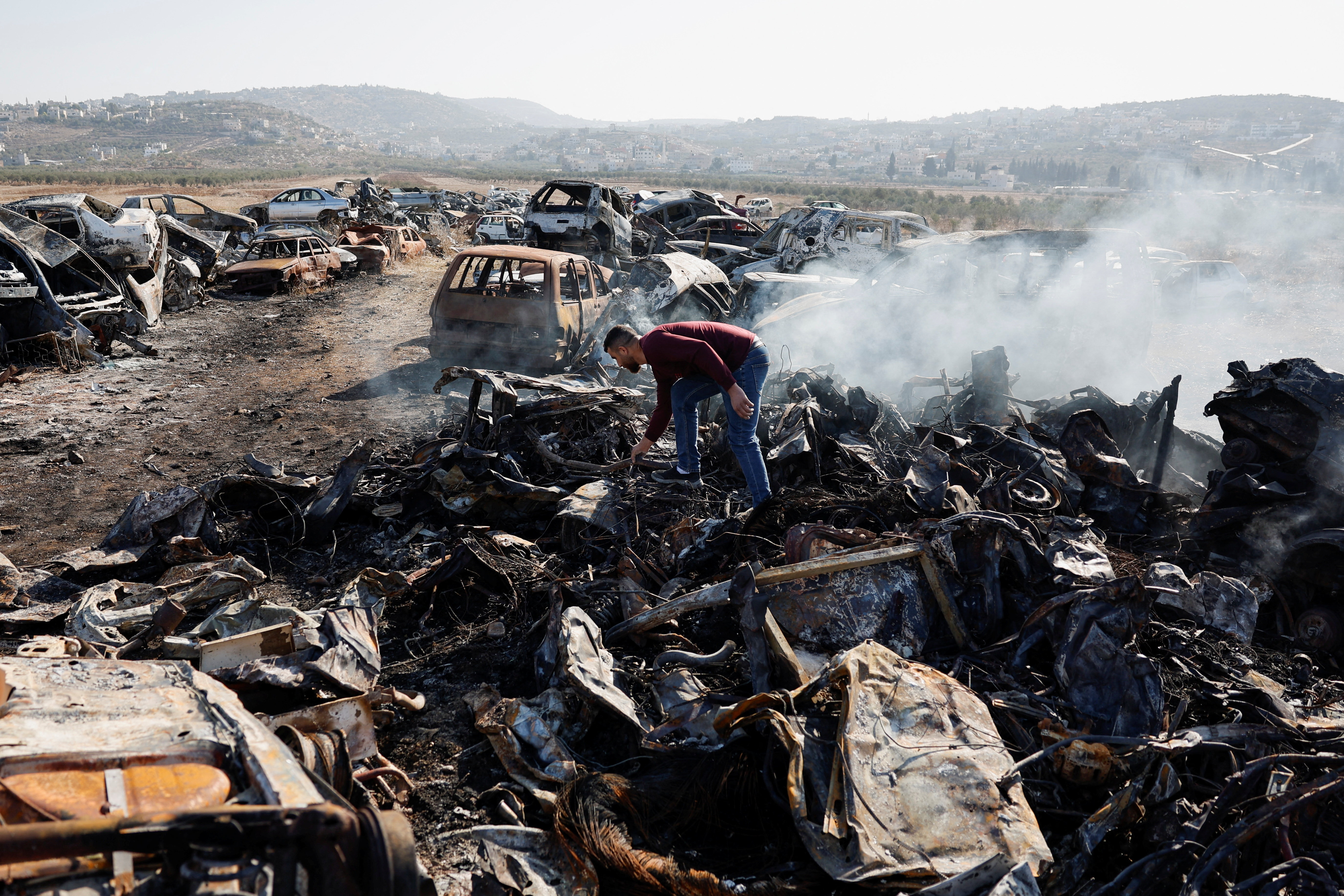 A Palestinian, Yahya Dalal, 32, inspects cars burnt in an attack by Israeli settlers, in Huwara in the Israeli-occupied West Bank, November 21, 2025. REUTERS/Ammar Awad