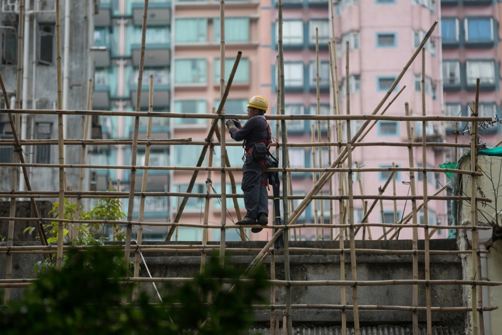 a worker in a hard hat stands on bamboo scaffolding near a high rise building