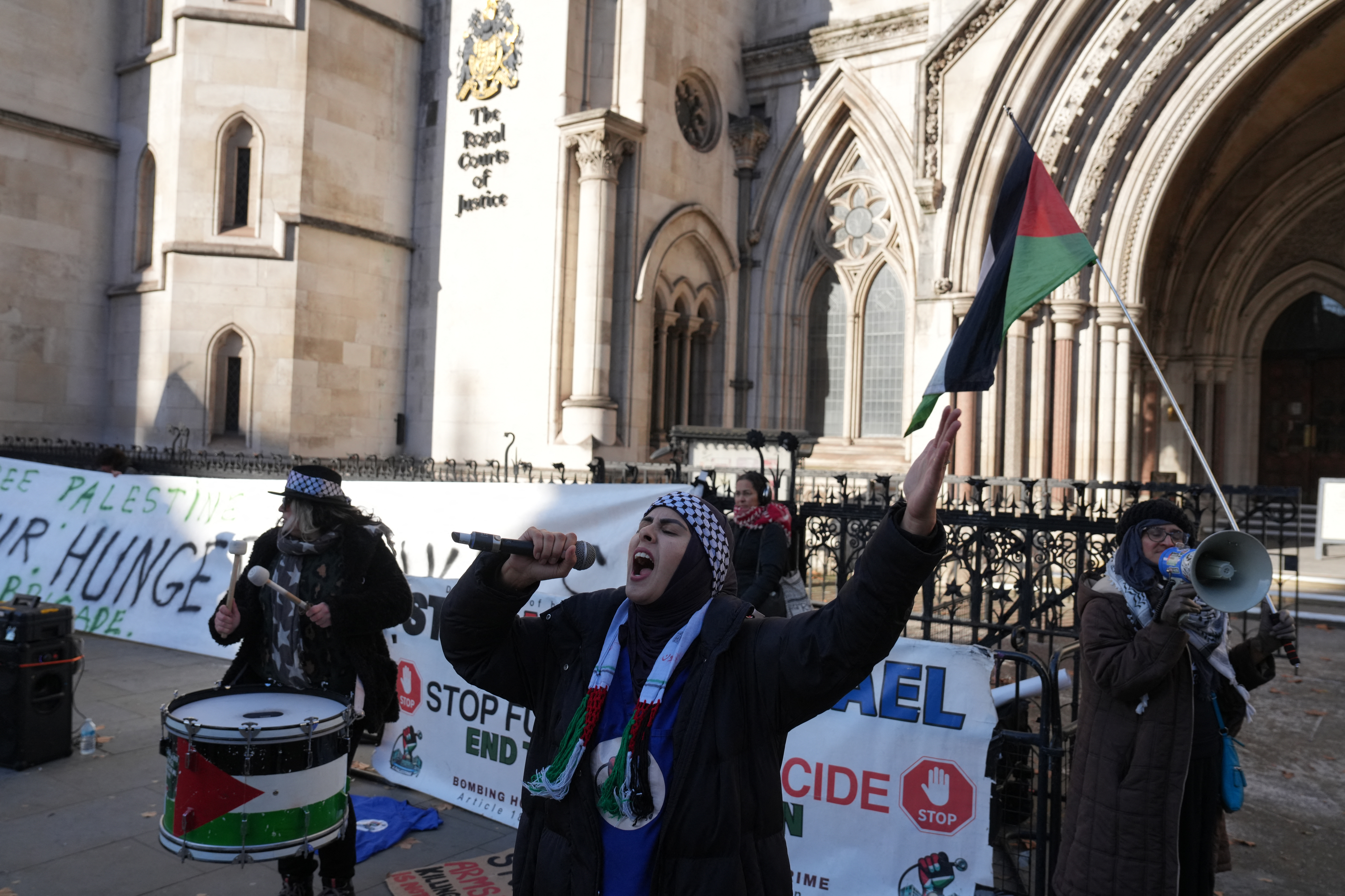 Protesters hold placards and flags during a demonstration in support of "Defend Our Juries" and their campaign against the ban on Palestine Action, outside the Royal Courts of Justice, Britain's High Court, in central London on November 26, 2025.