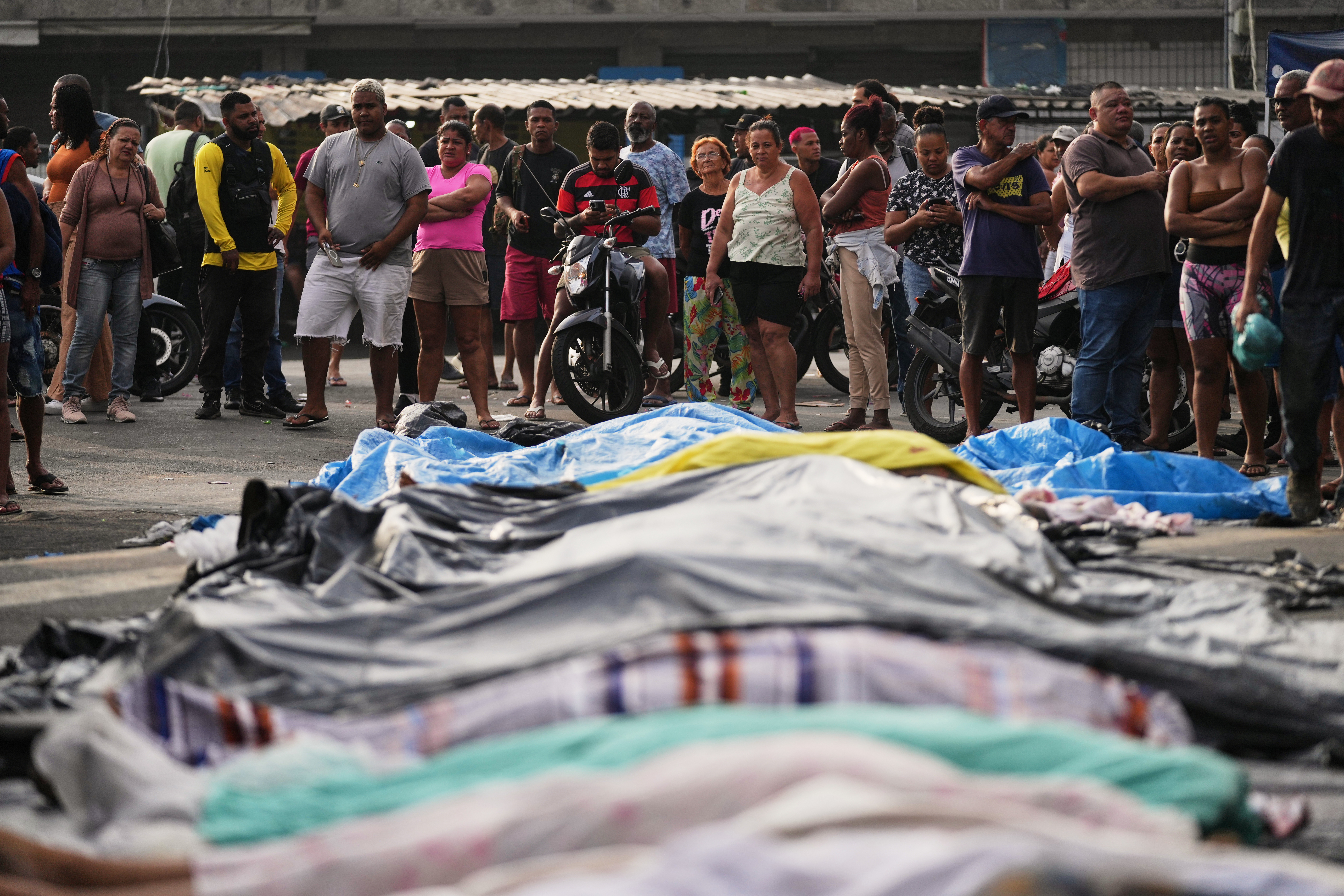 People look at the bodies lined up by residents of those killed the day before during a police raid targeting the Comando Vermelho gang in the Complexo da Penha favela of Rio de Janeiro, Brazil, Wednesday, Oct. 29, 2025..(AP Photo/Silvia Izquierdo)