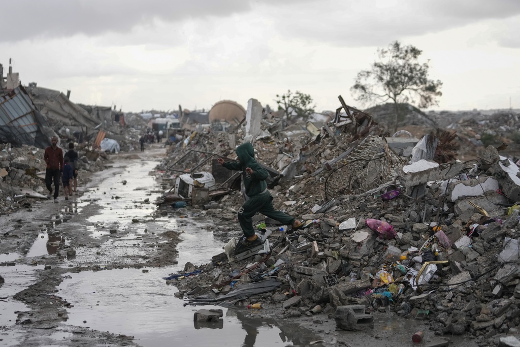 A stream of rain amid the rubble as a boy in a sweater tries to cross the street