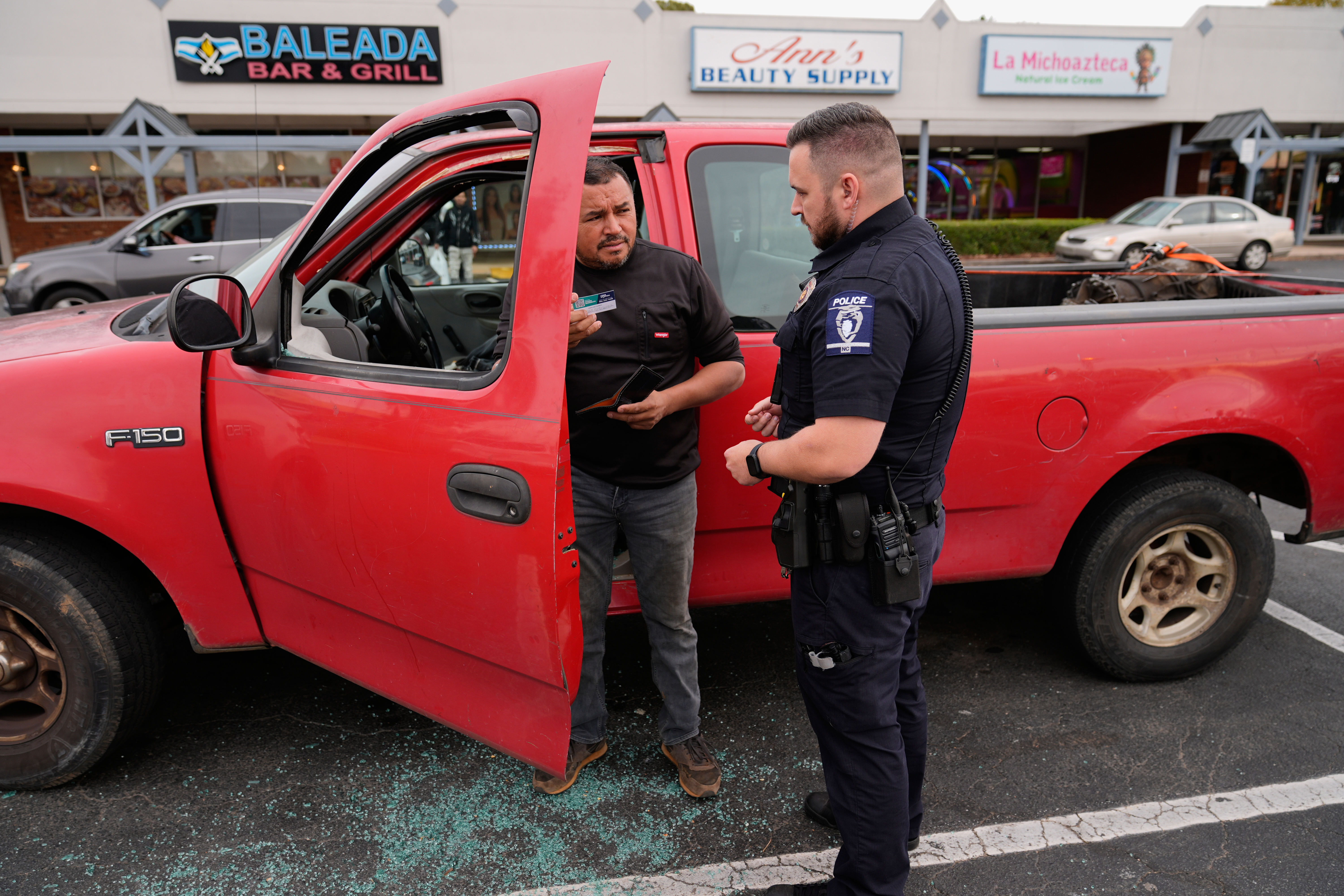 Willy Aceituno, left, makes a police report with Charlotte-Mecklenburg Police Department officer N. Sherill, after US Customs and Border Protection officers broke his window during an enforcement operation on November 15, 2025 in Charlotte, North Carolina.