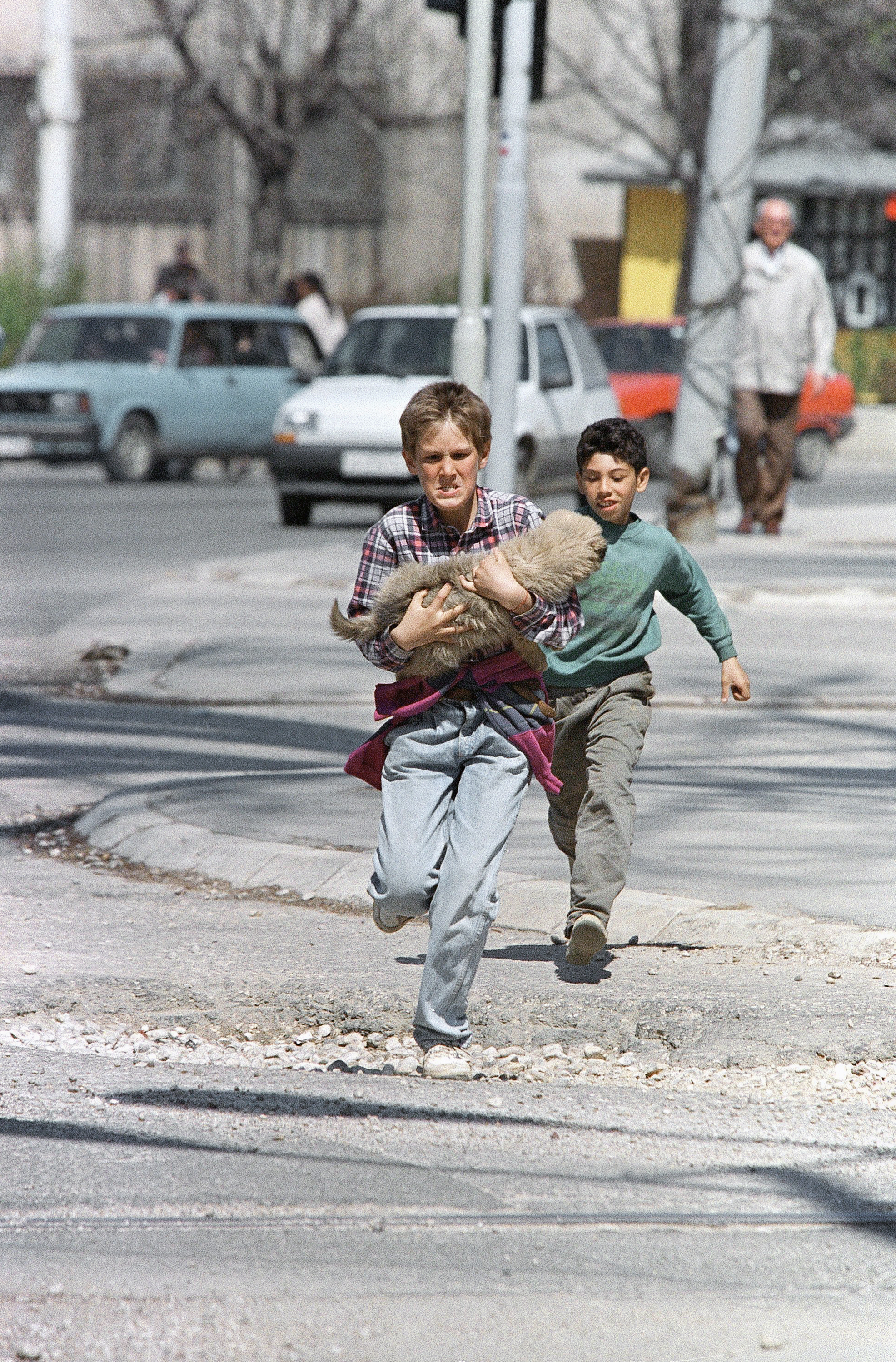 Carrying his dog, a boy springs across a central intersection which is sometimes targeted by snipers on Thursday