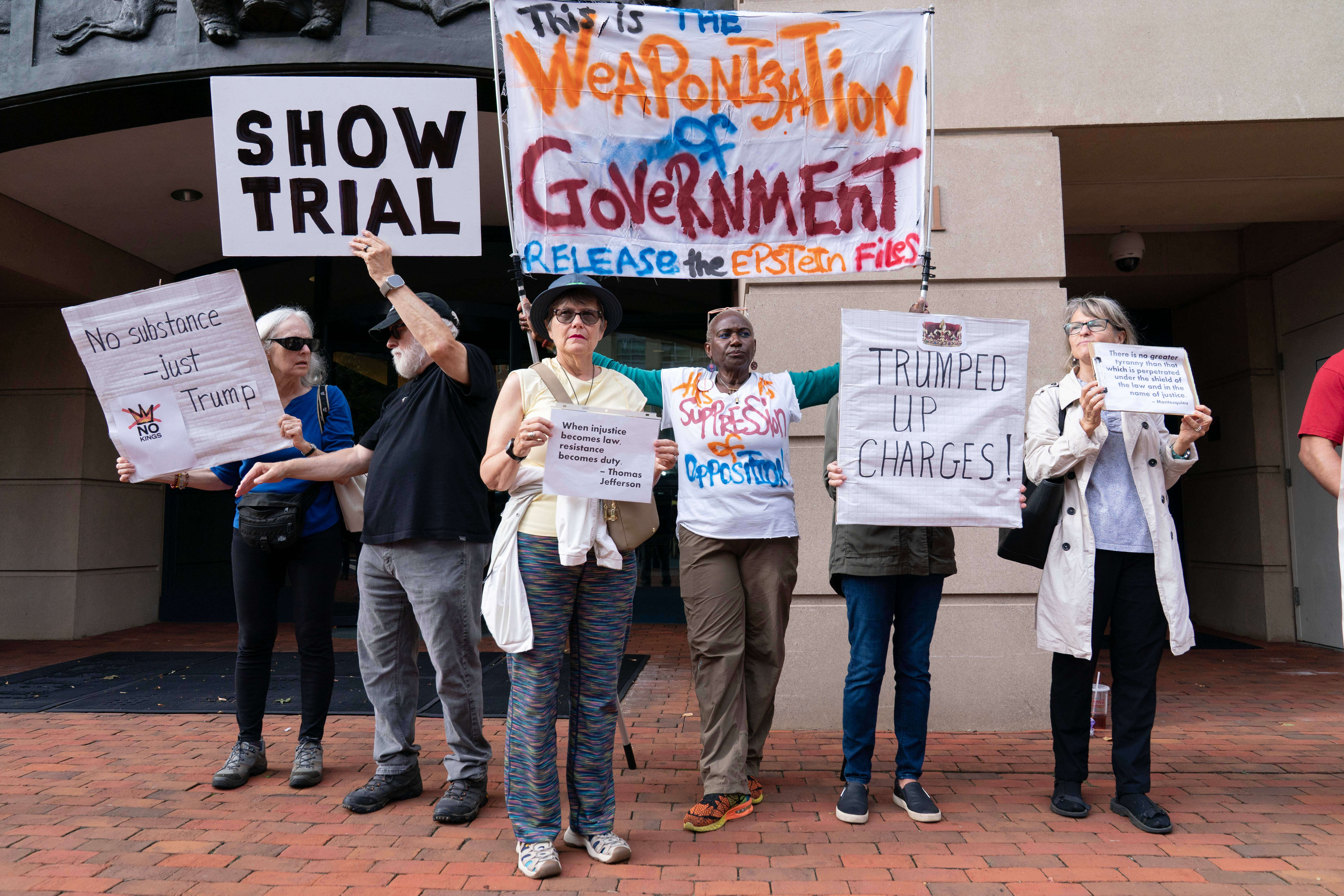 Protesters hold up signs that read, "Show trial" and "Weaponization of government"