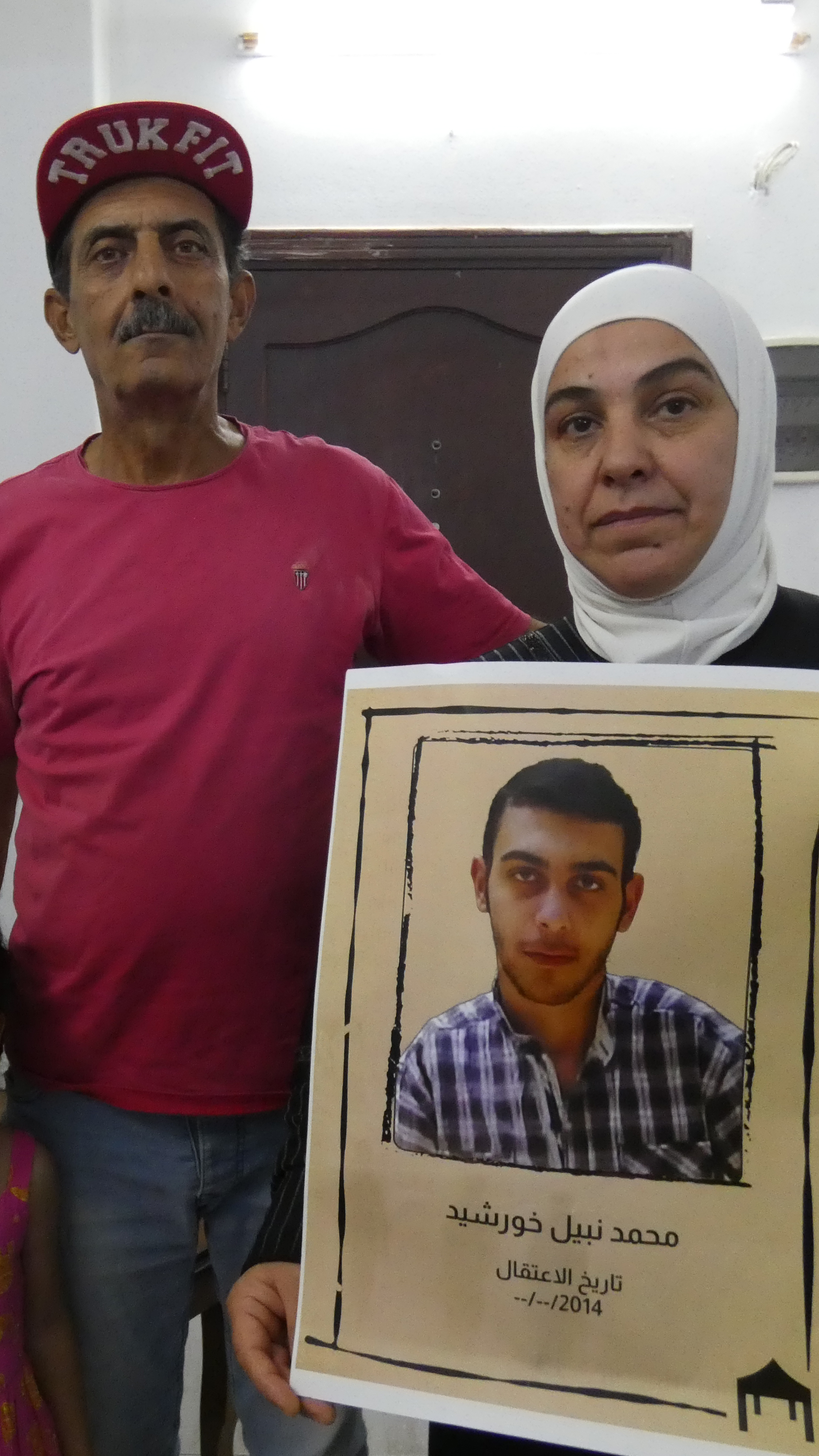 Safinaz Al Chaaibi, right, holds a picture of Hamid, with her husband Nabil, and their granddaughter Sham beside her [Caolan Magee/Al Jazeera]