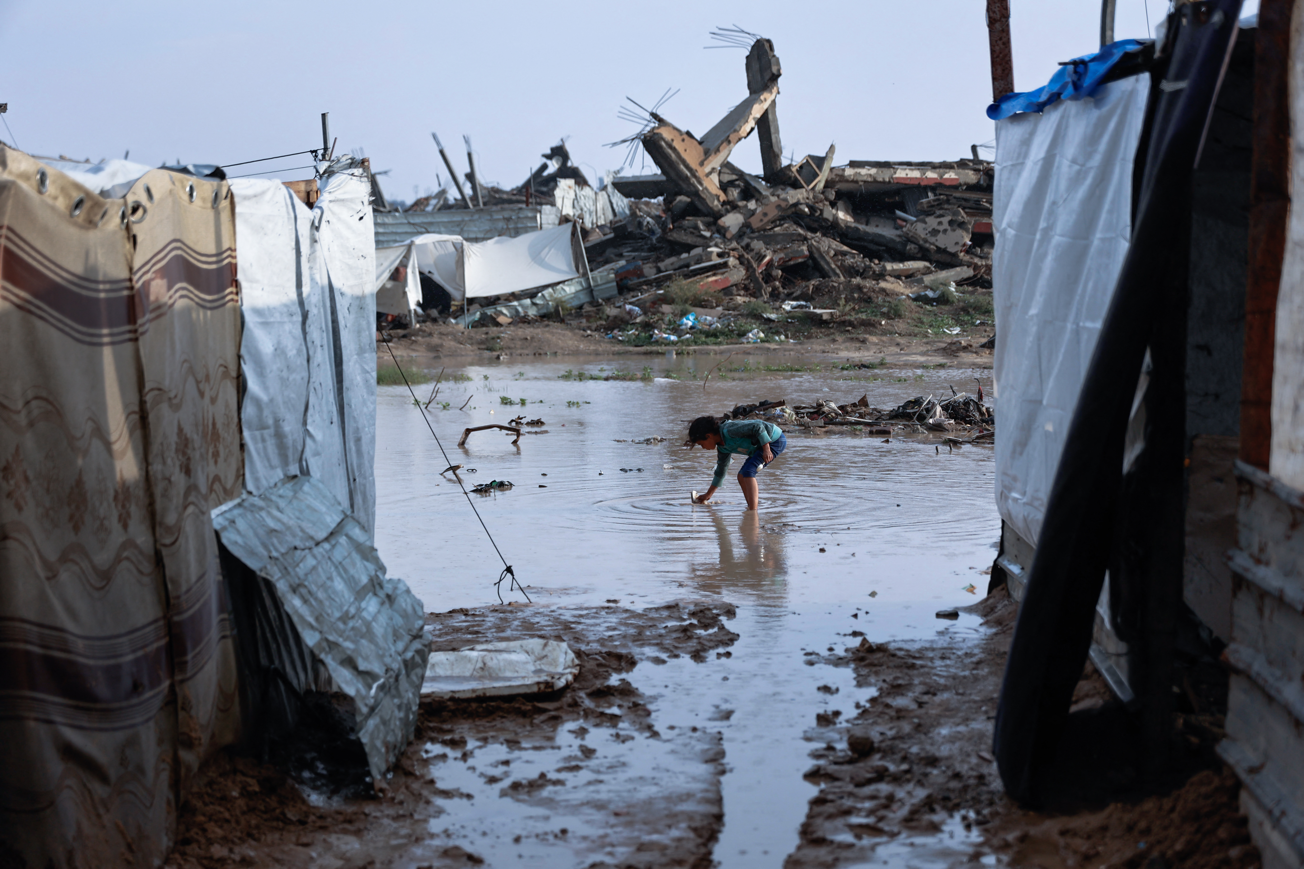 A girl stands in a pool of water at a makeshift camp sheltering displaced Palestinians after heavy rains in the Zeitoun neighbourhood of Gaza City on December 11, 2025.