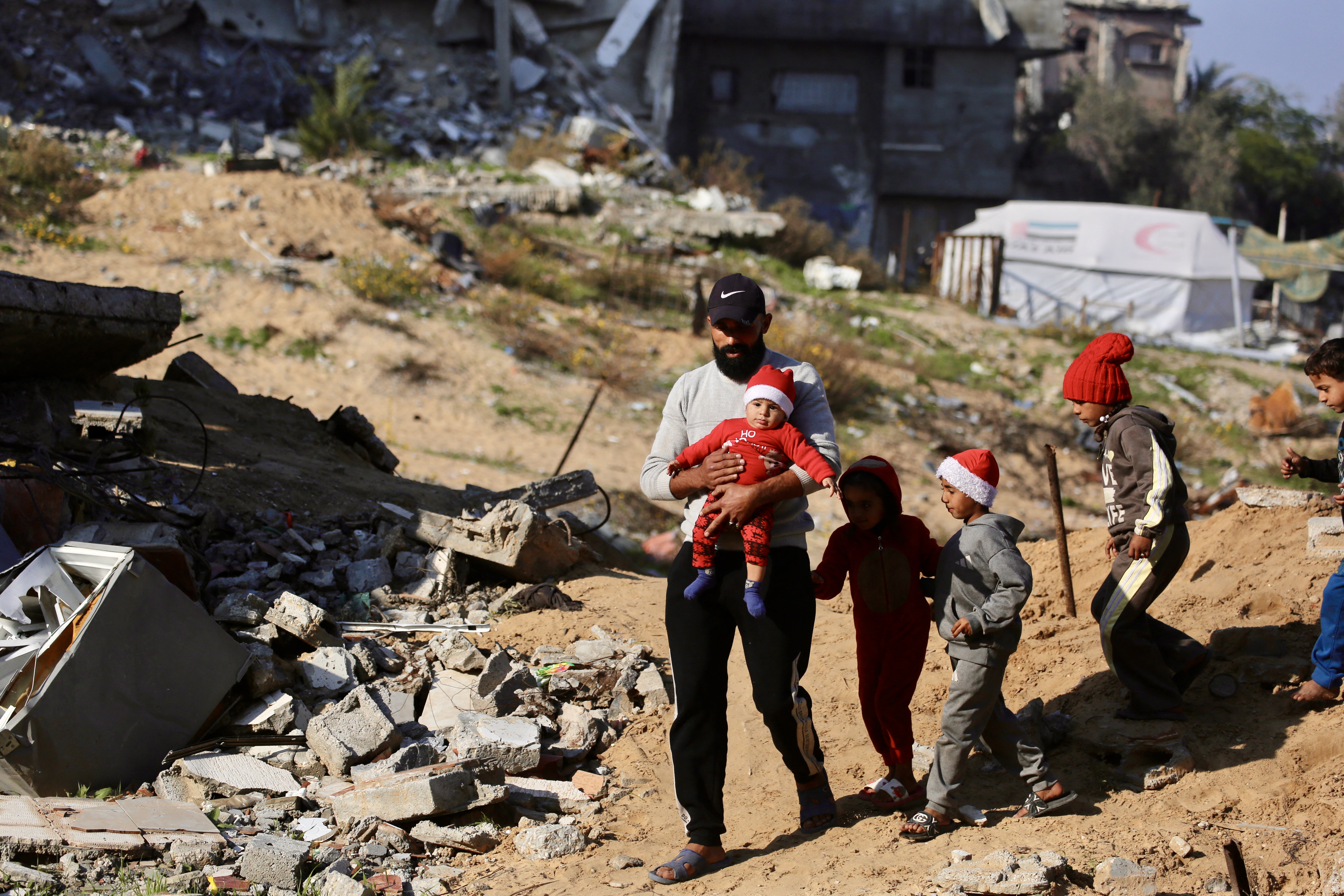 A Palestinian man walks with children next to the rubble of destroyed buildings in the Jabalia refugee camp, in the northern Gaza Strip on December 24, 2025. (Photo by Bashar Taleb / AFP)